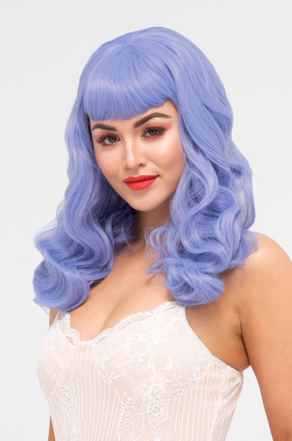 Woman with a blue wig wearing a white lace top on a light grey background. Long blue-purple wig with short fringe and old Hollywood waves: Ophelia