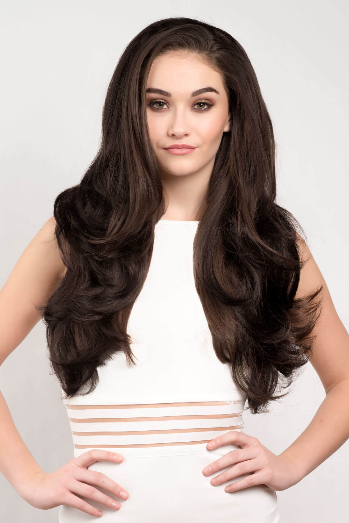 Woman with long, wavy brown hair wearing a white top with gold stripes on a light gray background. Reddish brown half wig hairpiece with long, gentle waves: Heather dark brown 6 and reddish brown 33