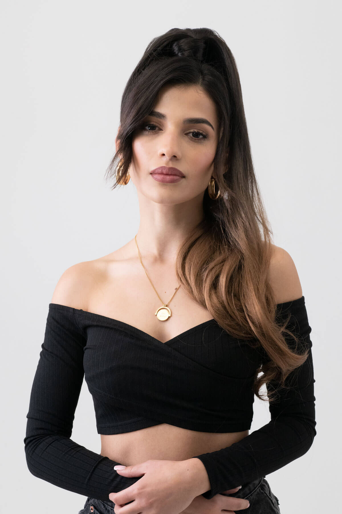 Woman wearing a black off-shoulder top with a plain background. Long ponytail extension with soft waves: Sophie brown to blonde ombre 4TN27