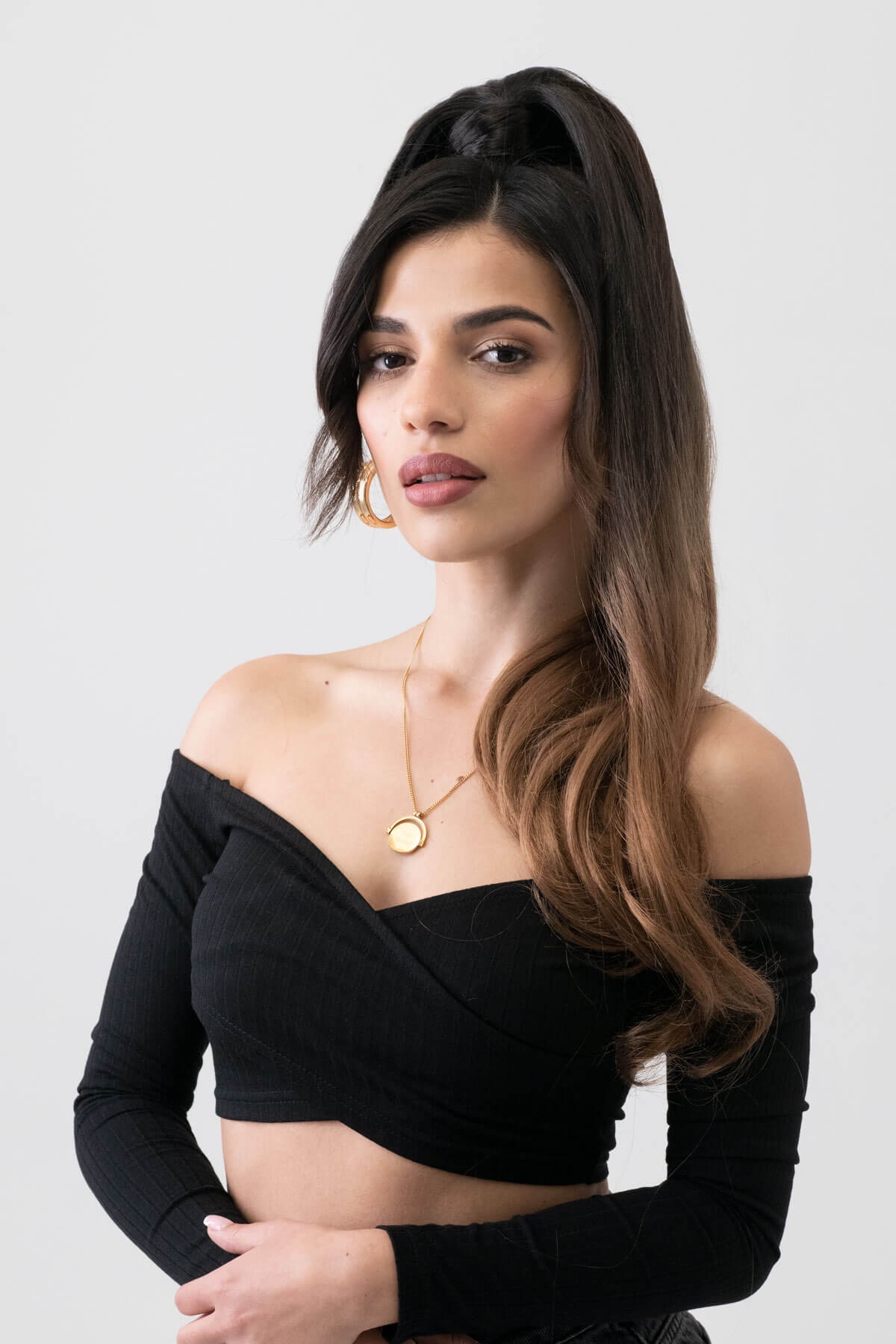 Woman wearing a black off-shoulder top with a plain background. Long ponytail extension with soft waves: Sophie brown to blonde ombre 4TN27