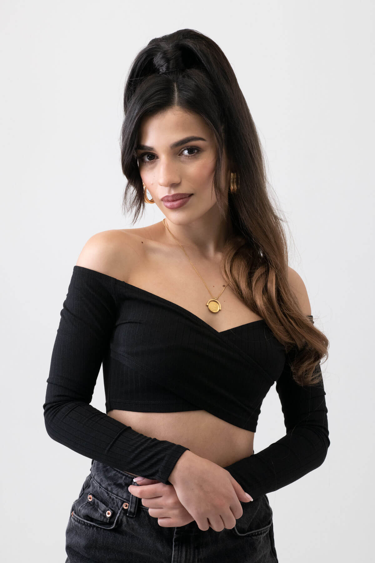 Woman wearing a black off-shoulder top against a white background. Long ponytail extension with soft waves: Sophie brown to blonde ombre 4TN27