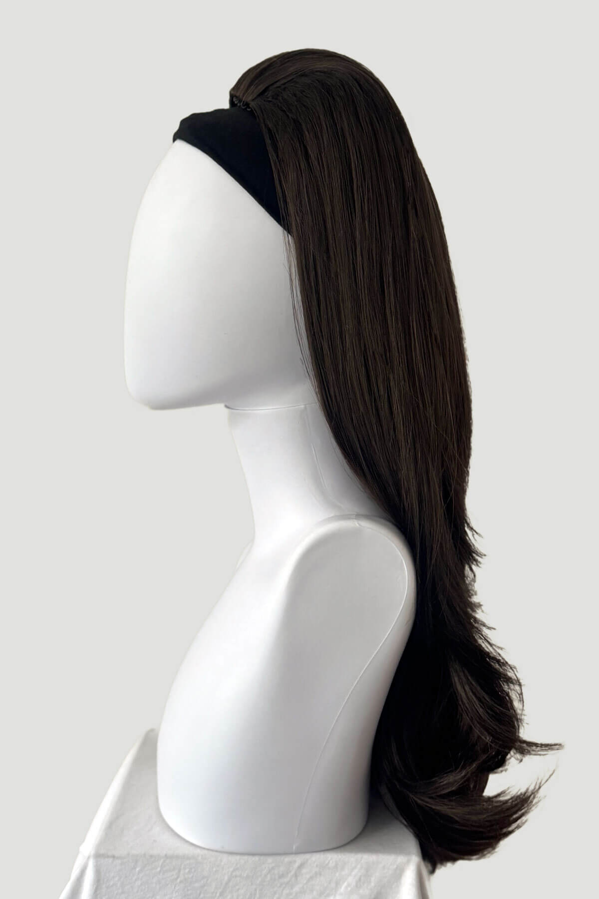 Mannequin head with long dark brown hair styled in a ponytail on a white background. 1960s style hair, high crown long straight and layered half wig: Juliette dark brown 6