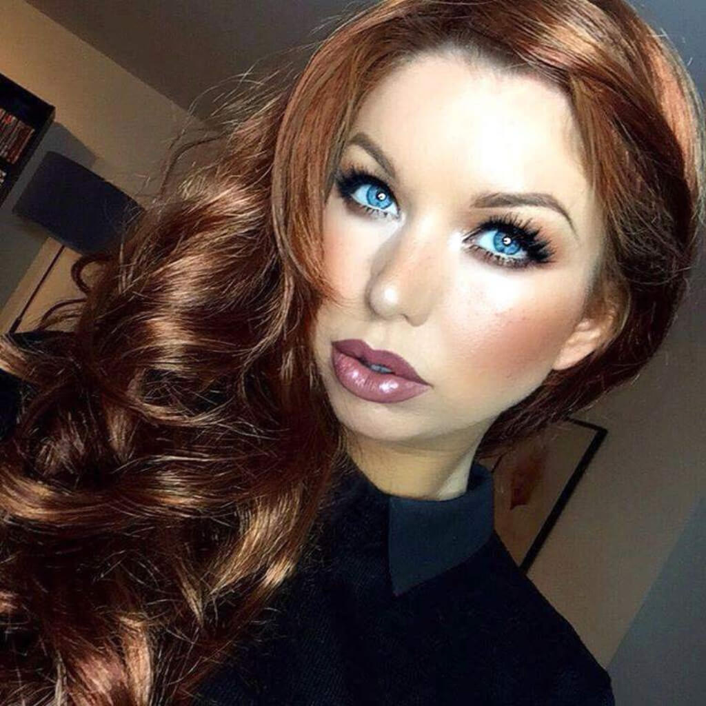 Person with long wavy hair and blue eyes posing indoors. Red & auburn wig with blonde highlights, long: Freya