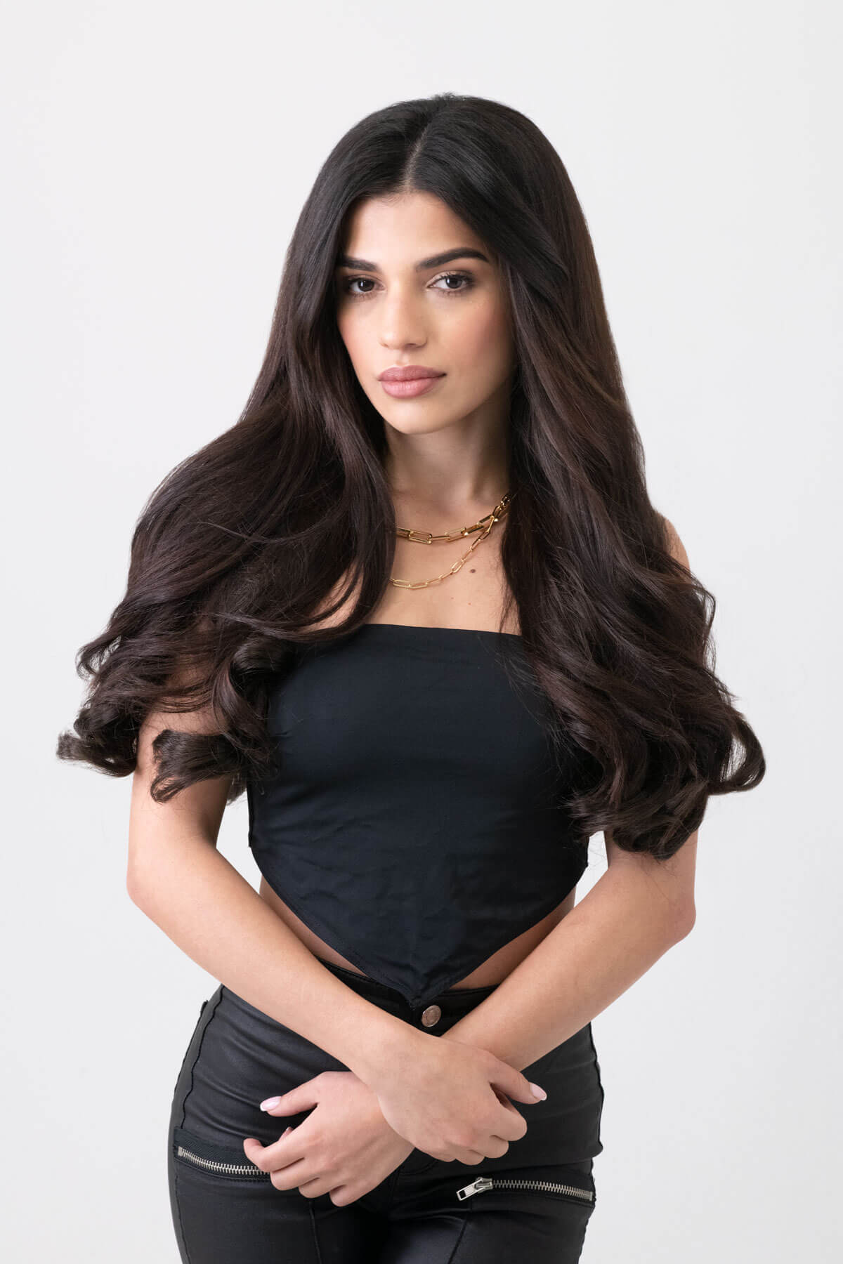 Woman with long, wavy hair wearing a black outfit on a white background. 5 piece synthetic hair extension set, 18 inches long, 260g
