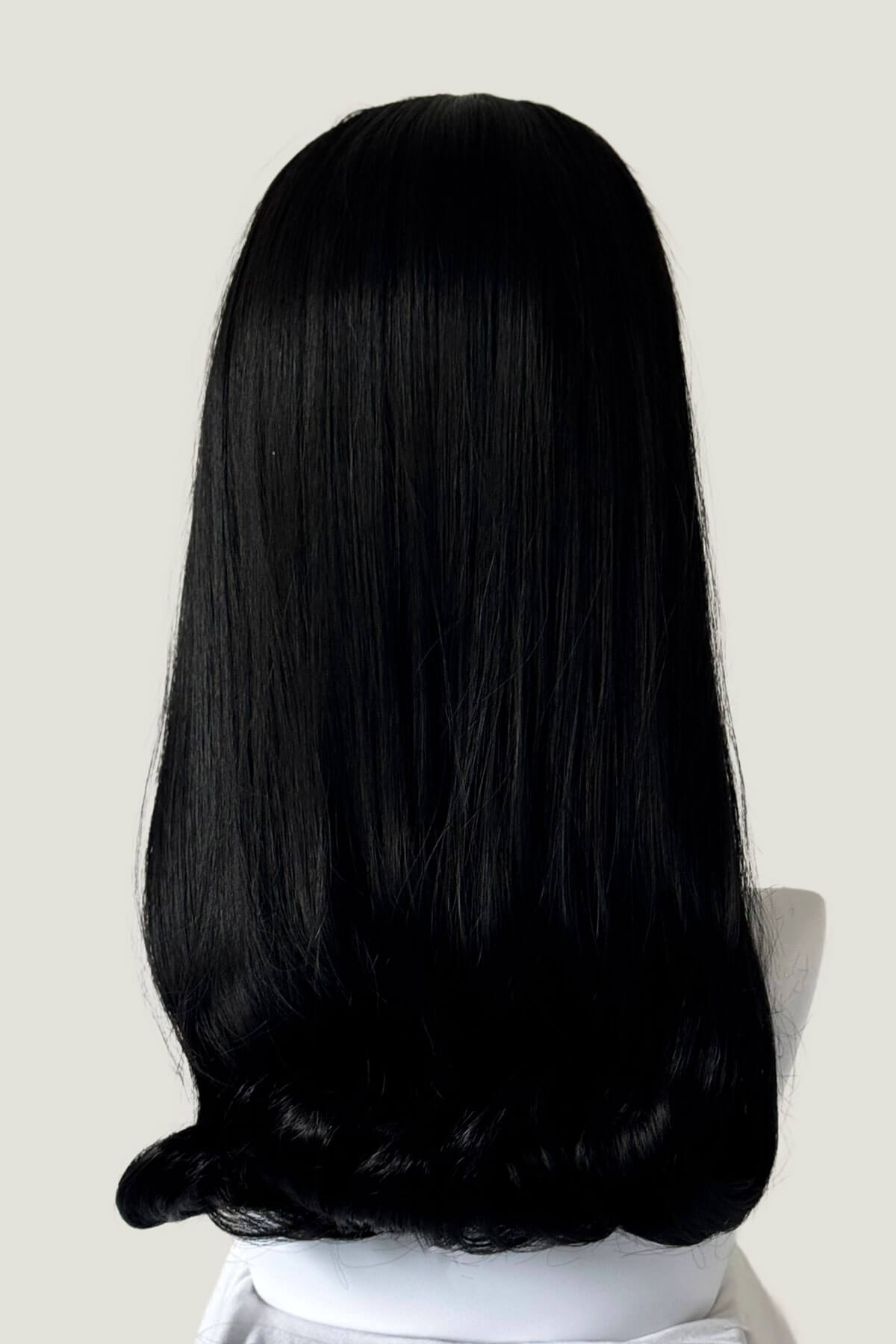 Person with long black hair sitting against a plain background. 1960s Retro high crown, half wig hairpiece, long with hair flip: Priscilla black 1b
