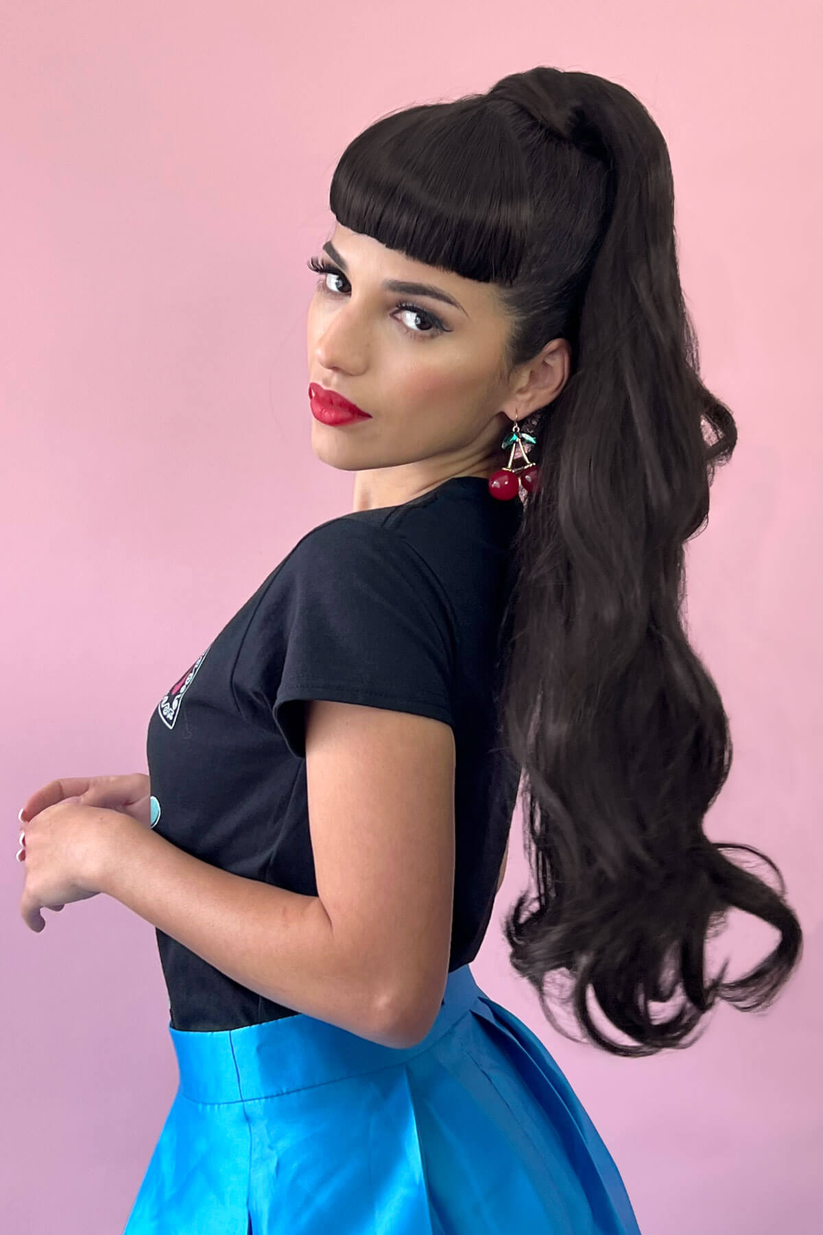 Woman with long dark hair styled in a high ponytail against a pink background.Long ponytail extension with soft waves: Sophie 613T24