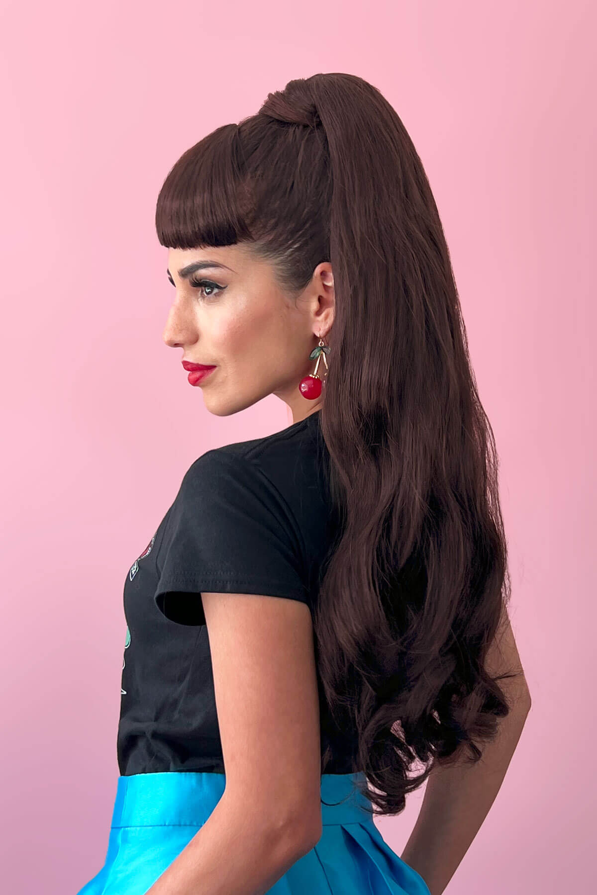 Woman with long dark hair styled in a high ponytail against a pink background. Long ponytail extension with soft waves: Sophie chestnut brown 8
