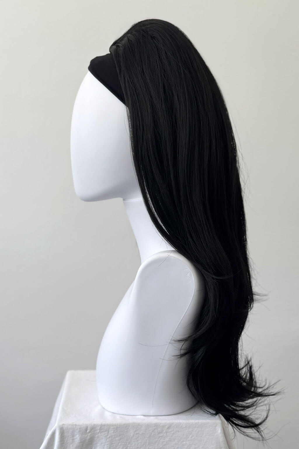 Black wig on a mannequin head against a plain background. 1960s style hair, high crown long straight and layered half wig: Juliette black 1b