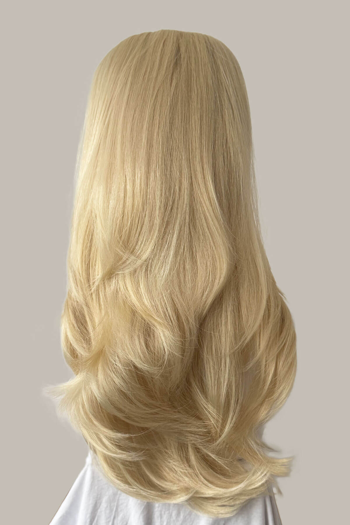 Blonde wig on a mannequin head against a neutral background. 1960s style hair, high crown long straight and layered half wig: Juliette champagne blonde 613