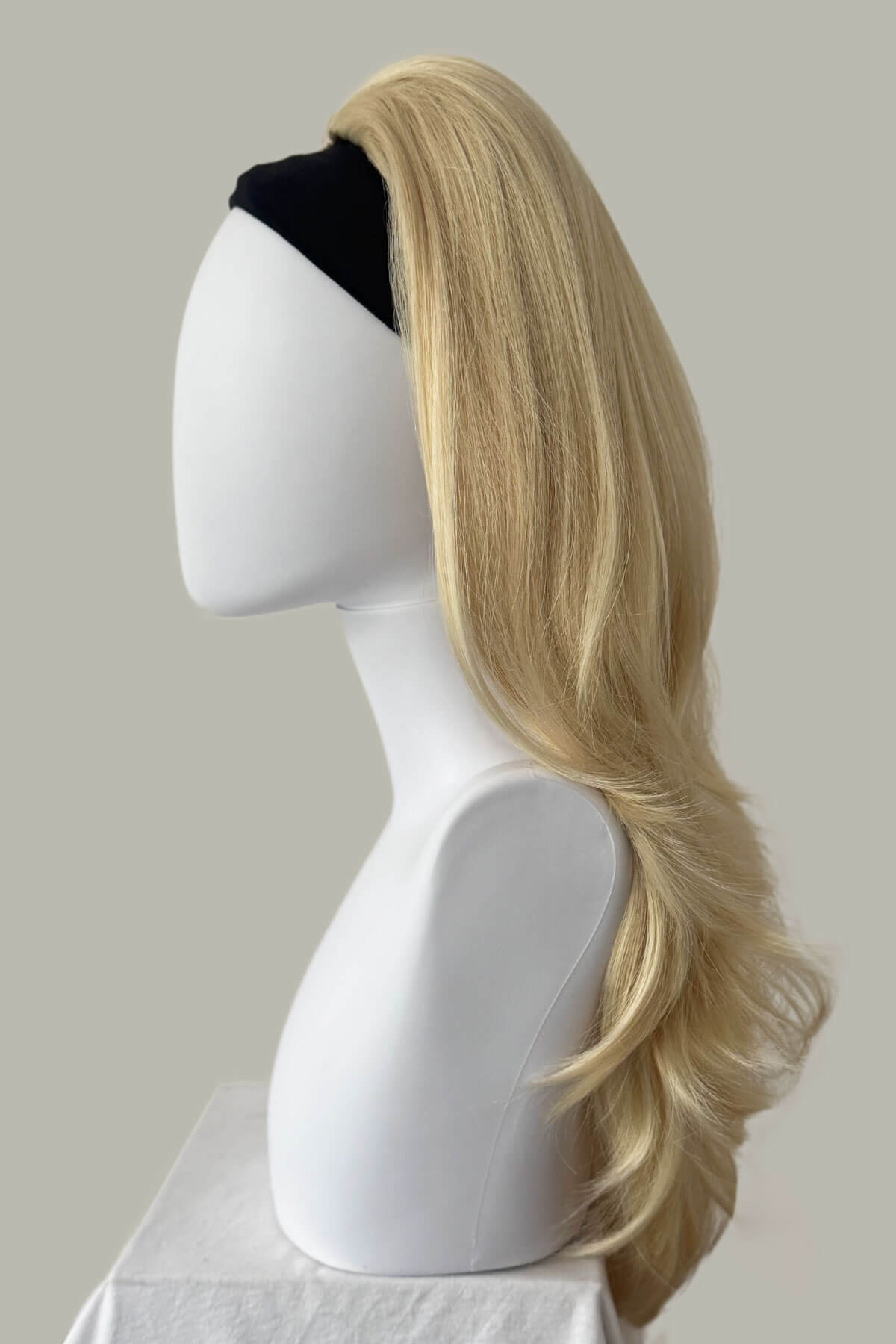 Blonde wig on a mannequin head against a plain background. 1960s style hair, high crown long straight and layered half wig: Juliette champagne blonde 613