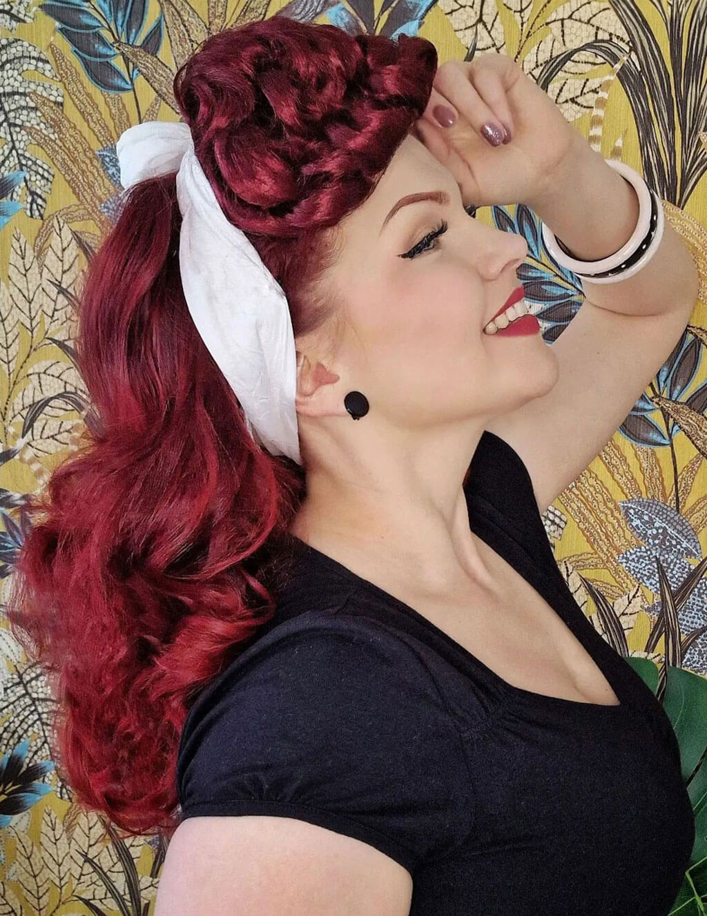 Woman with red hair styled in an elegant updo against a decorative background. Hair poodle clip-in hairpiece bun vintage style 1950s: Lucille cherry red 39