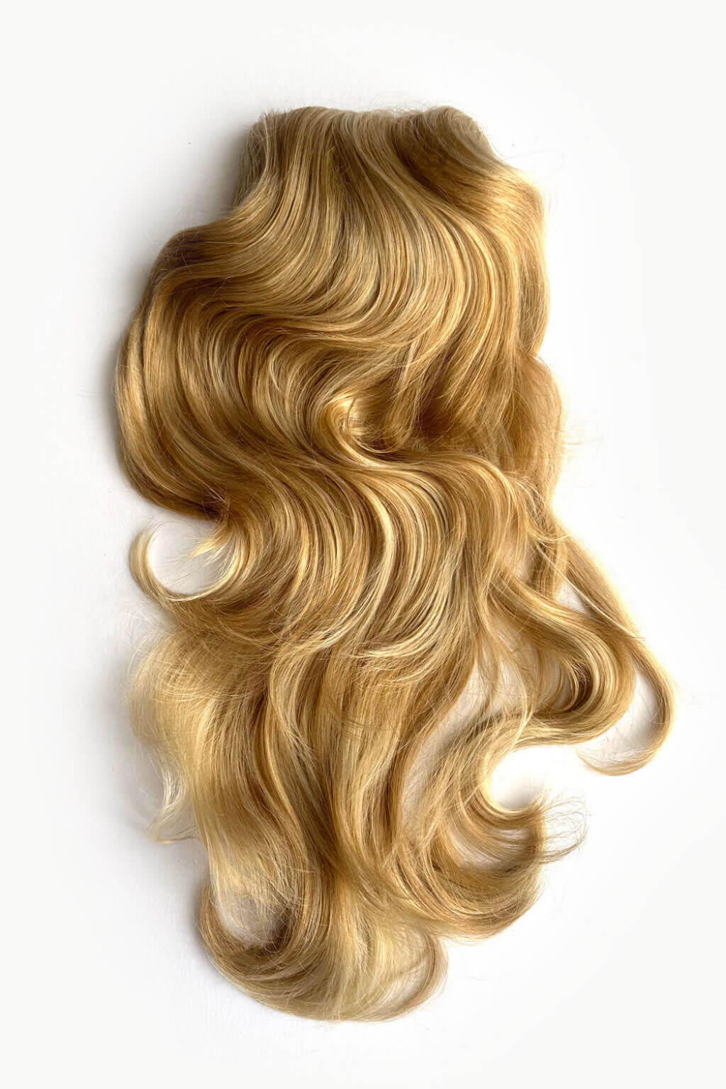 Long, wavy blonde hair extension or wig piece laid flat on a plain white background. Double volume hairpiece extension: Naomi warm blonde 24BH613