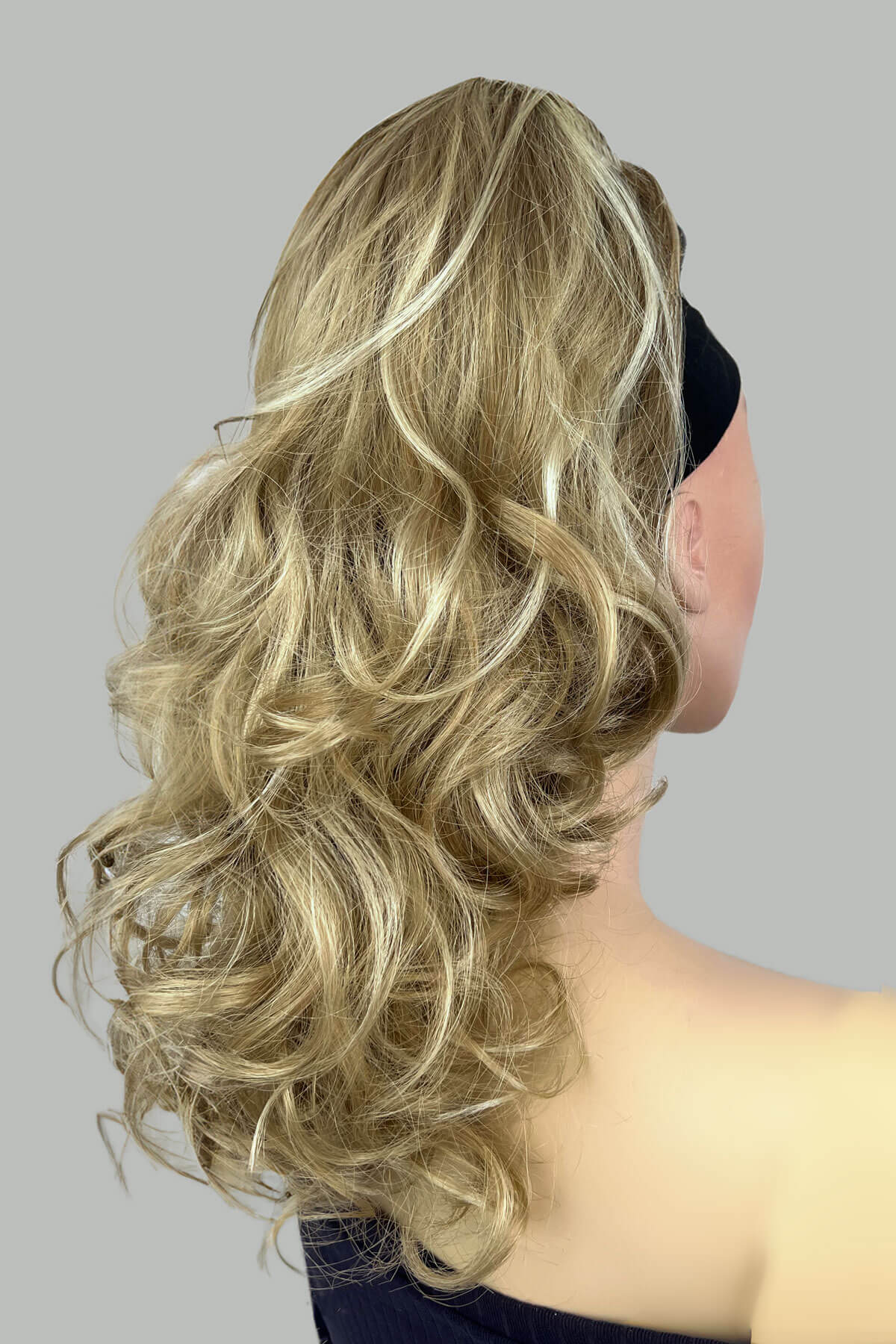 A woman wearing a floral off-shoulder top with a curly ponytail hairpiece extension in dark brown colour. blonde 24H613