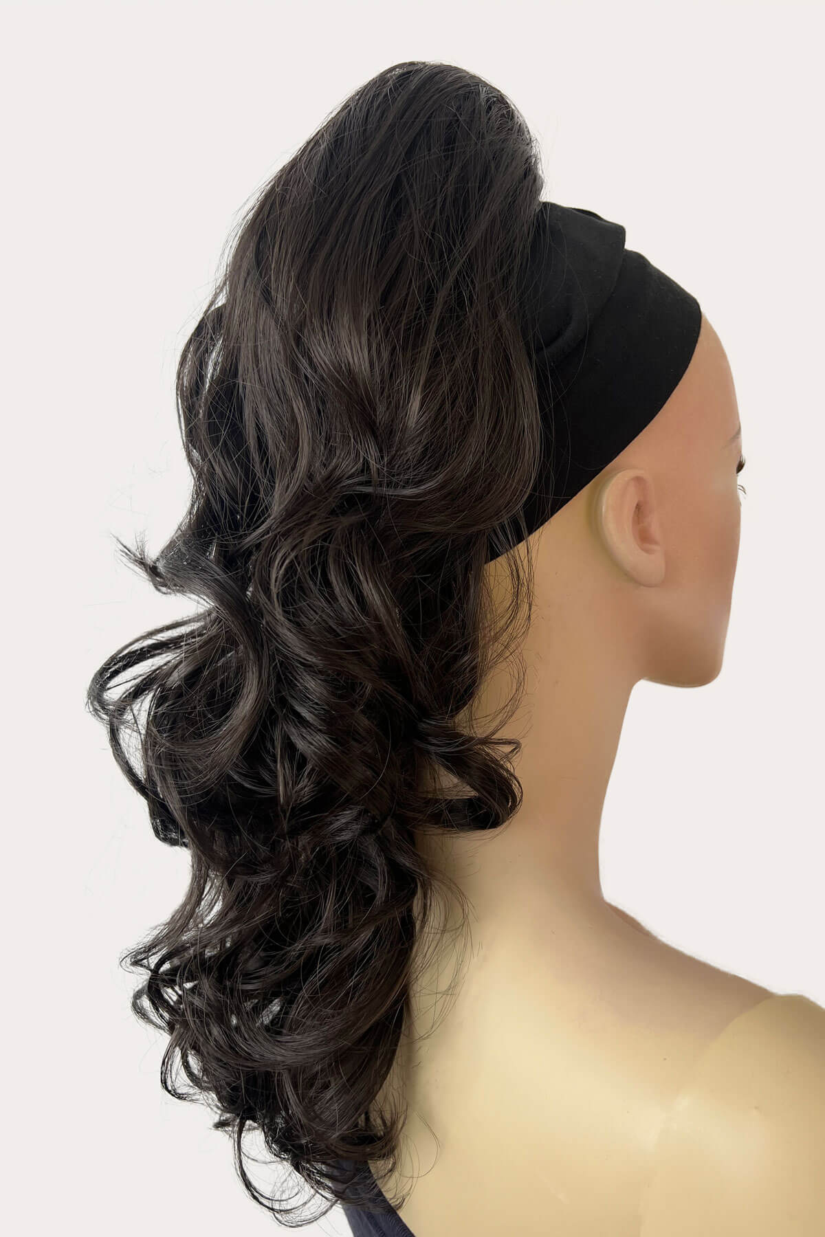 A woman wearing a floral off-shoulder top with a curly ponytail hairpiece extension in dark brown colour. Curly ponytail hairpiece extension: Katy dark brown 4