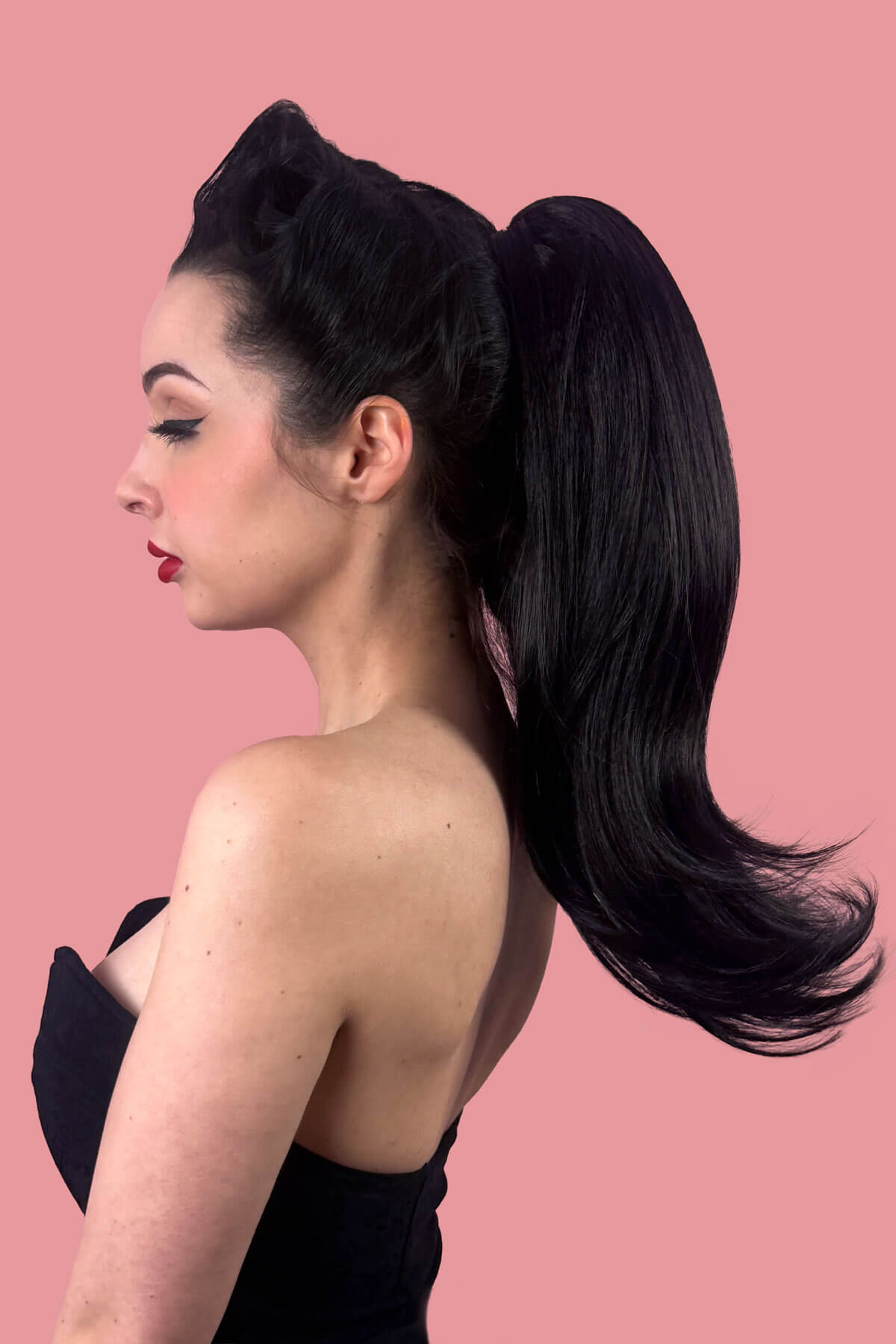 Woman with a long, black, high ponytail against a pink background. Long ponytail hairpiece, straight with flick: Clarisa black 1B