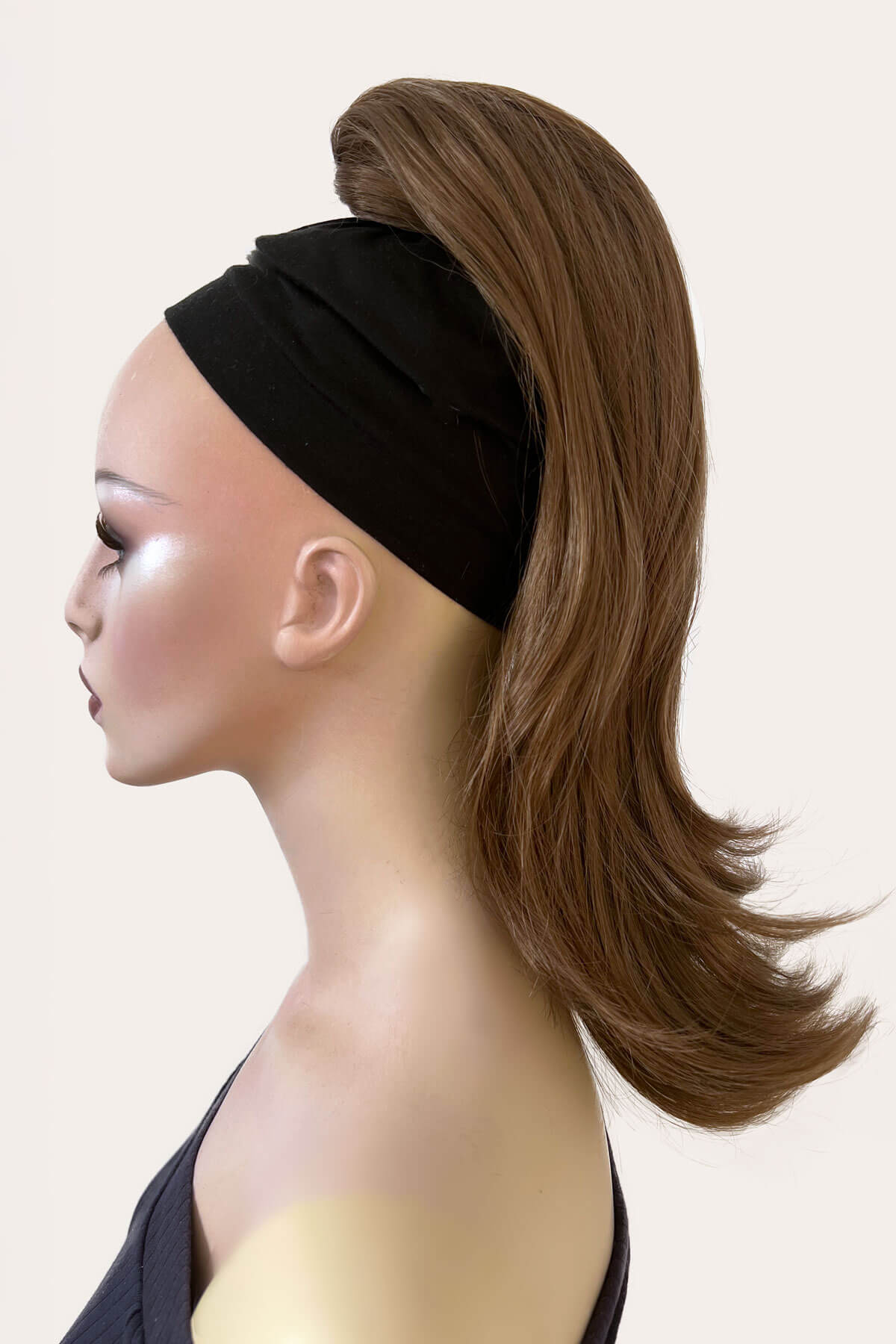 Mannequin head with brown hair styled in a ponytail wearing a black headband on a beige background. brown 12