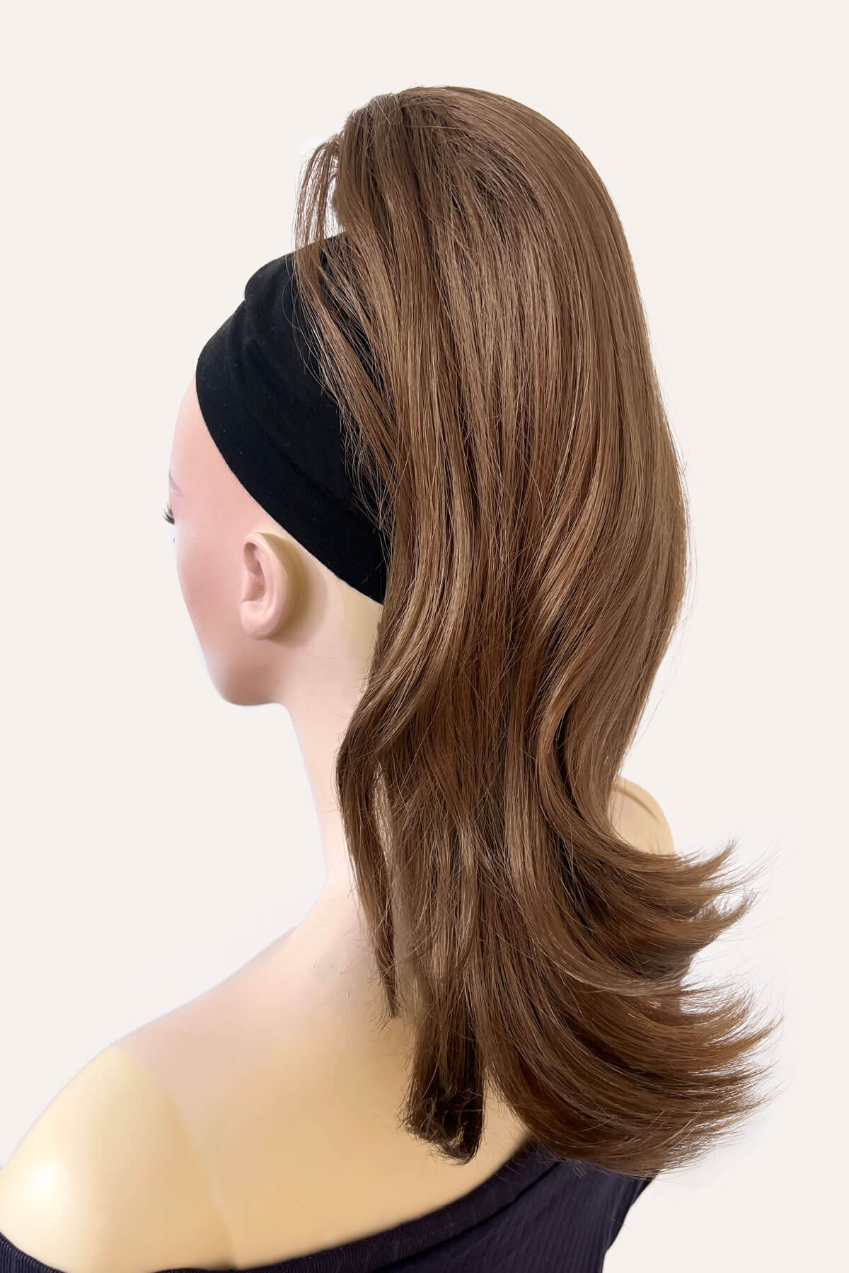Mannequin head with brown hair styled in a ponytail wearing a black headband on a beige background. brown 12