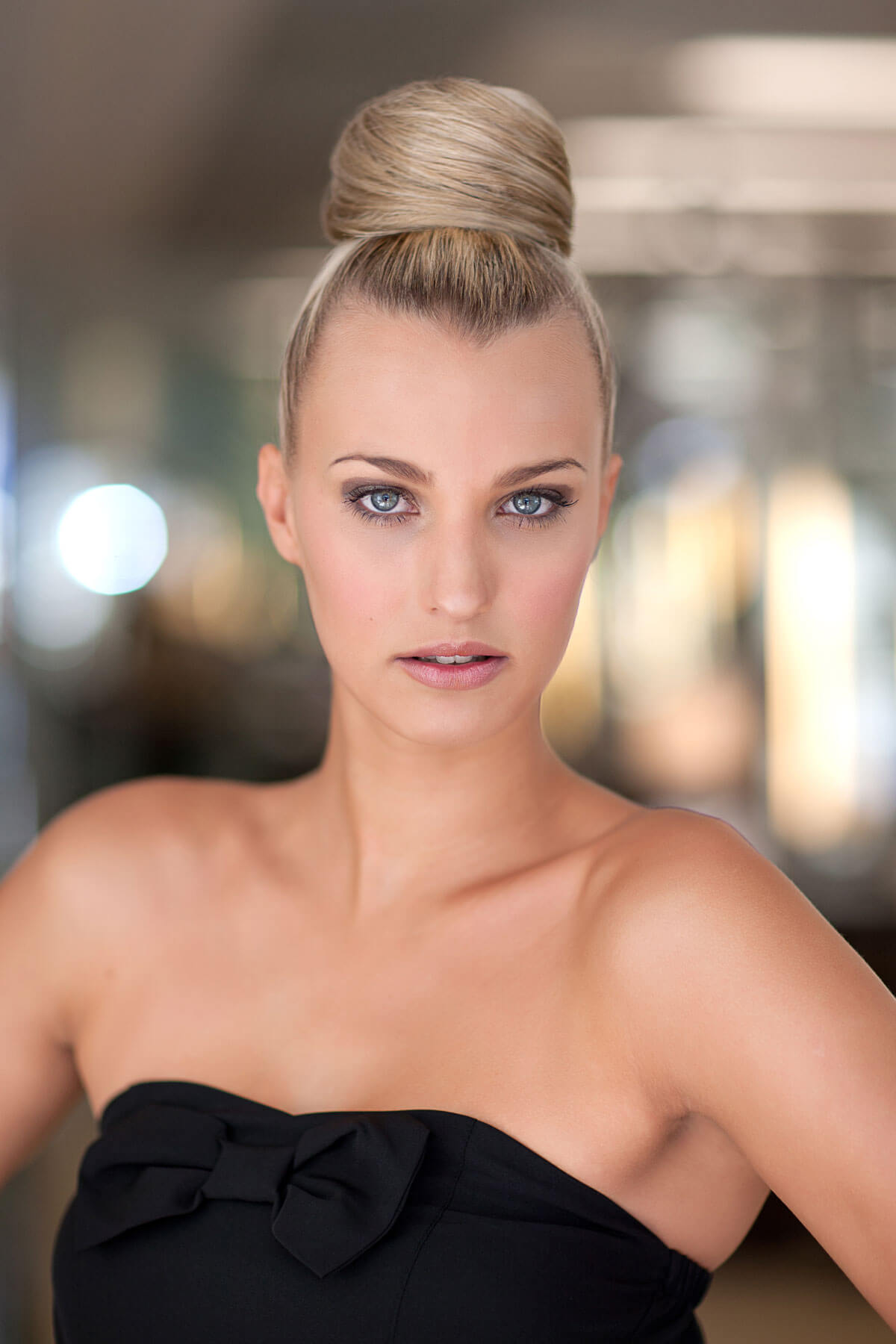 Woman with styled hair wearing a black strapless dress against a blurred background