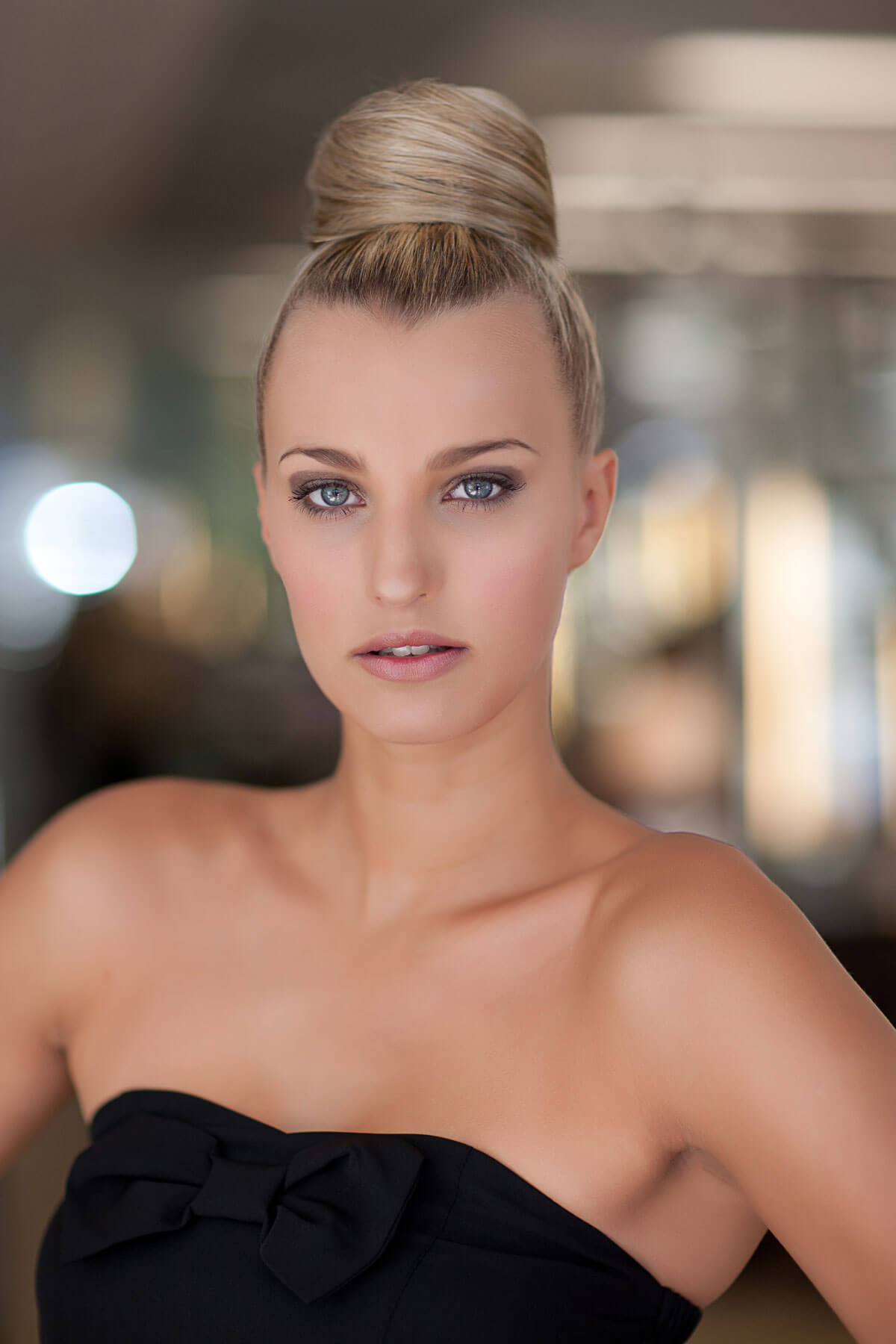 Woman with styled hair wearing a black strapless top against a blurred background. Hair bun hairpiece; instant perfect hairbun: Hebe