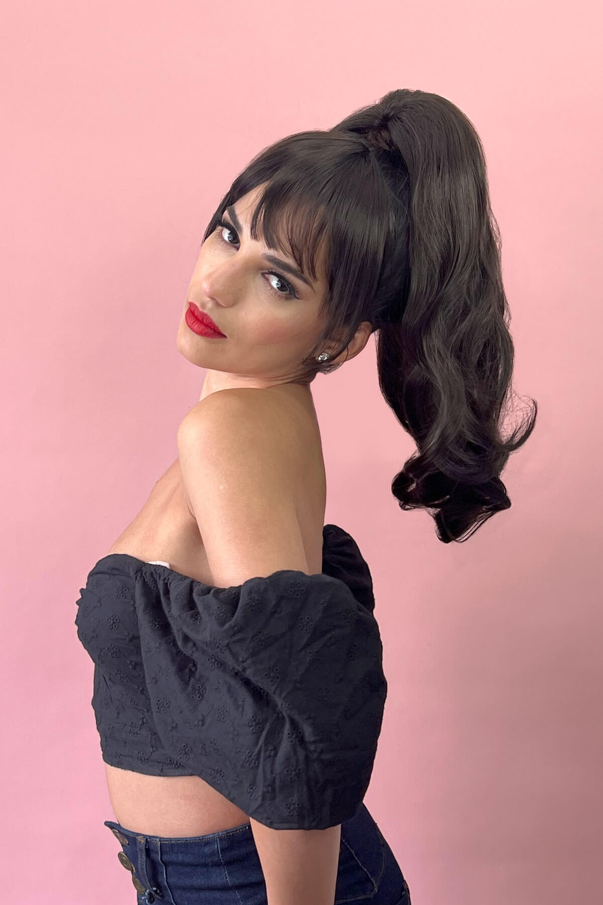 A woman wearing a black, wavy, layered ponytail hairpiece with a claw clip. Ponytail hairpiece extension, layered with waves: Elsa