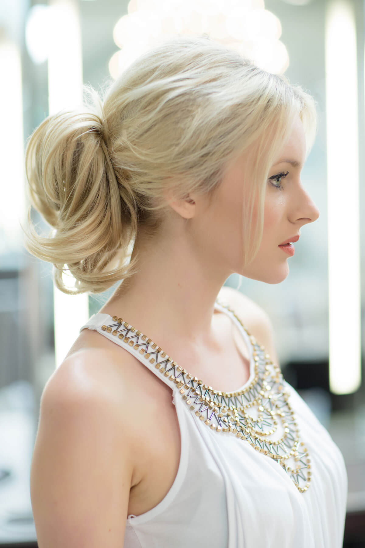 Woman with styled hair wearing a white top with a decorative neckline. Clip in hairpiece, ponytail, short, flexihair: Leela blonde 24H613