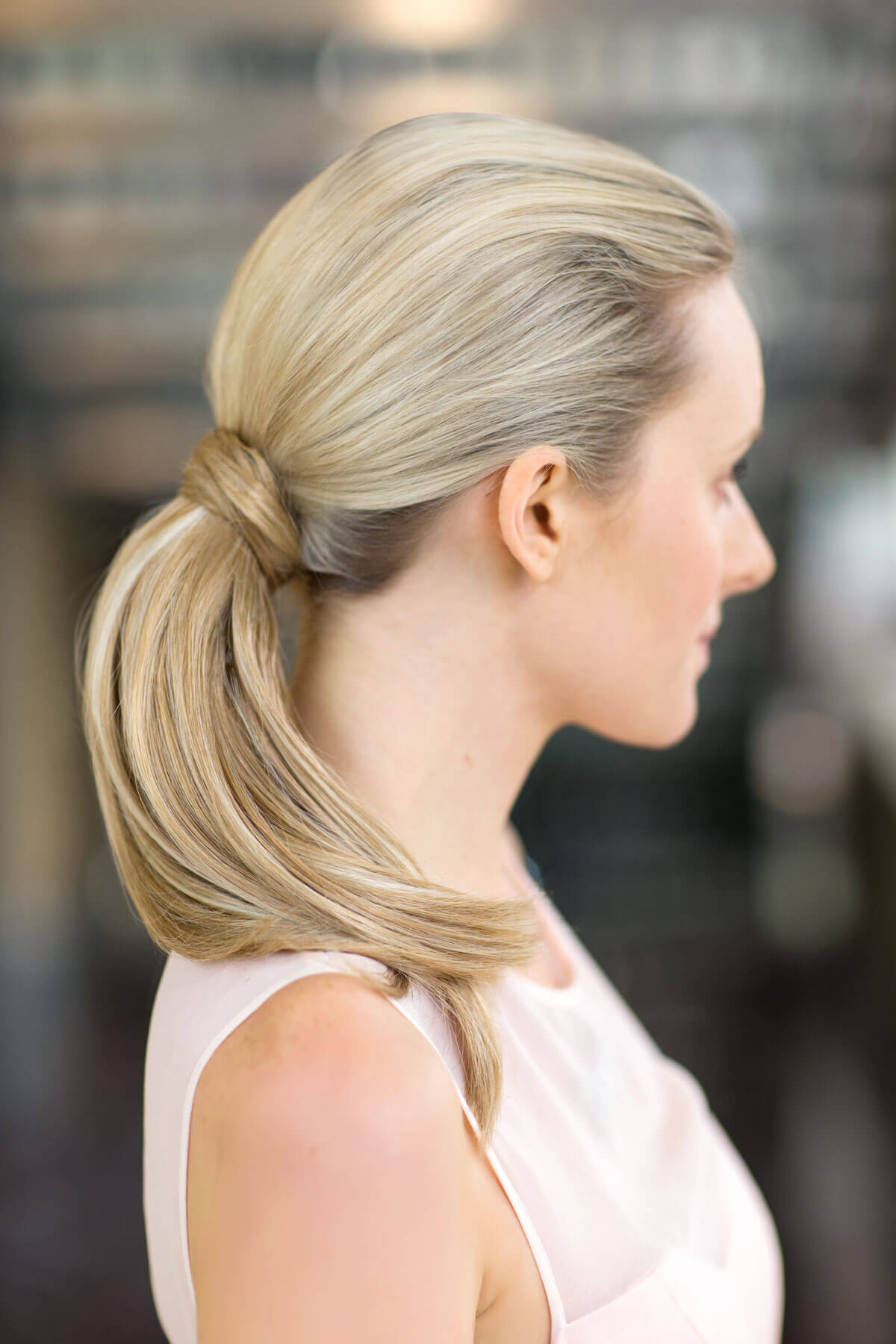 Woman with blonde hair styled in a ponytail against a blurred background