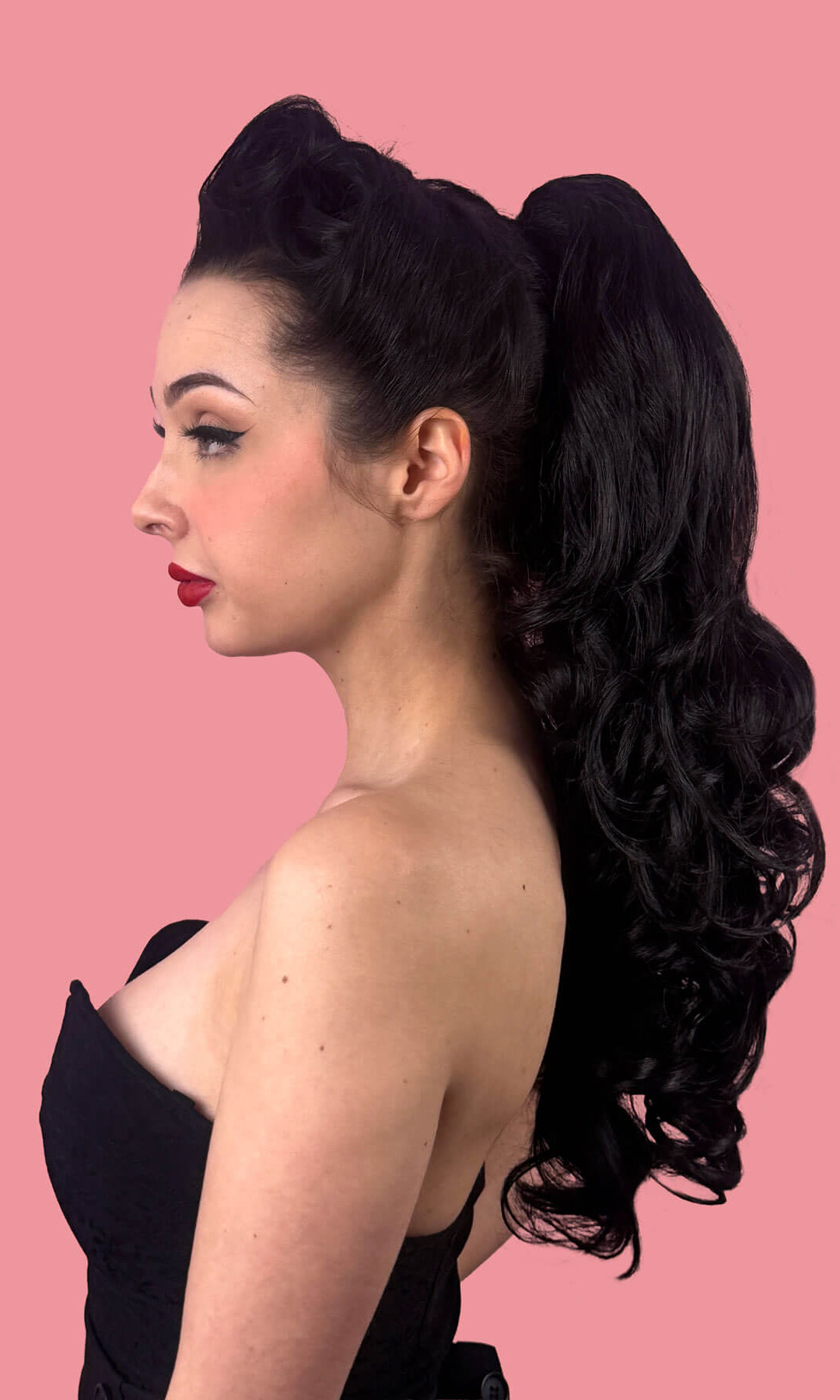 Woman in a black dress with red lipstick against a pink background. Long wavy ponytail hairpiece extension: Tiffany black 1B