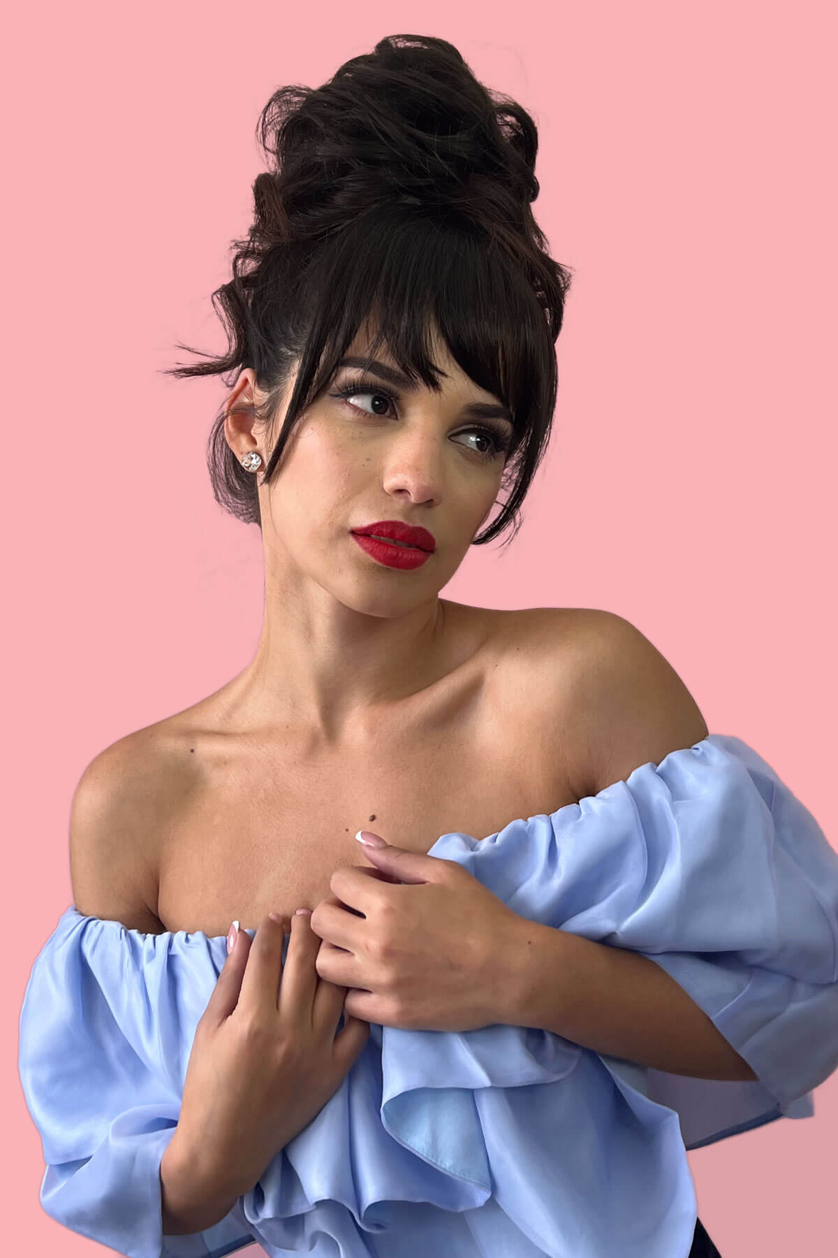 Woman with black hair wearing a light blue off-shoulder top against a pink background. Scrunchie bun hairpiece, easy updo messy bun: Betsy black 1b