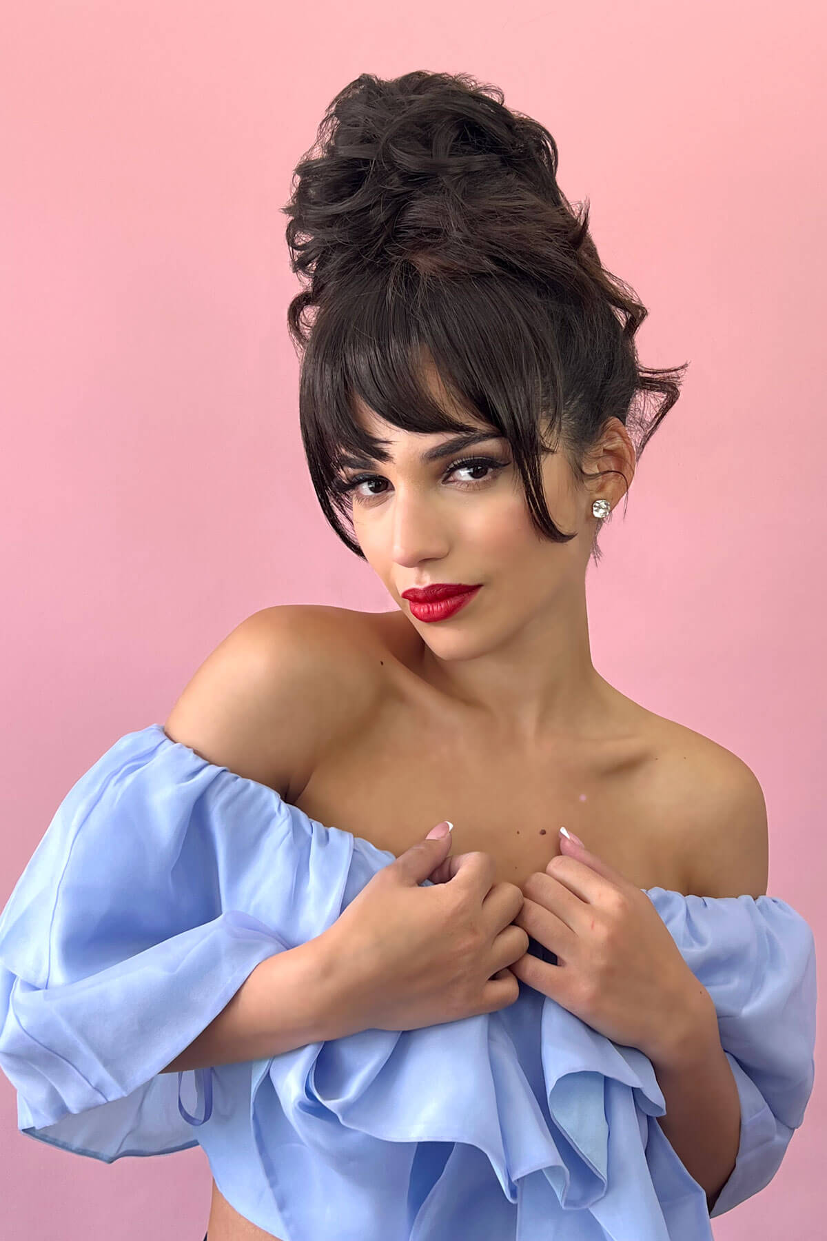 Woman with styled hair and red lipstick wearing a light blue off-shoulder top against a pink background. Scrunchie bun hairpiece, easy updo messy bun: Betsy colour brown 27