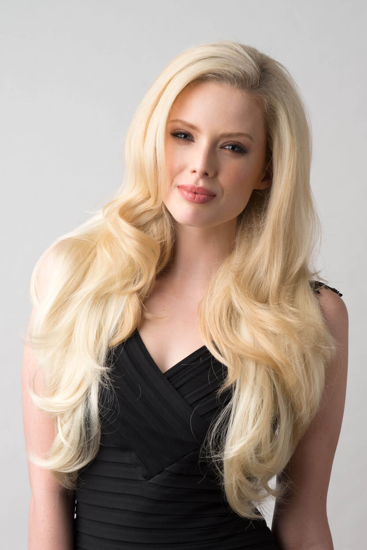 Woman with long blonde hair wearing a black dress against a gray background. Long blonde half wig hairpiece (3/4 wig) loose curls: Frankii creamy blonde 613