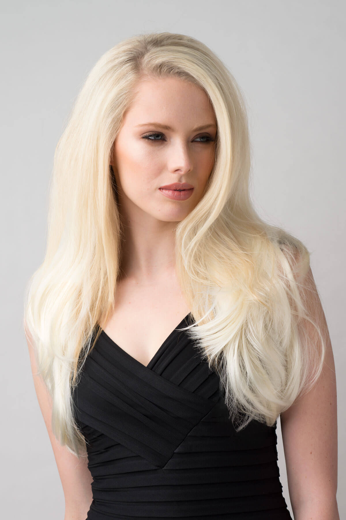 Woman with long blonde hair wearing a black dress against a gray background. Platinum blonde half wig hairpiece (3/4 wig), straight: Gwen