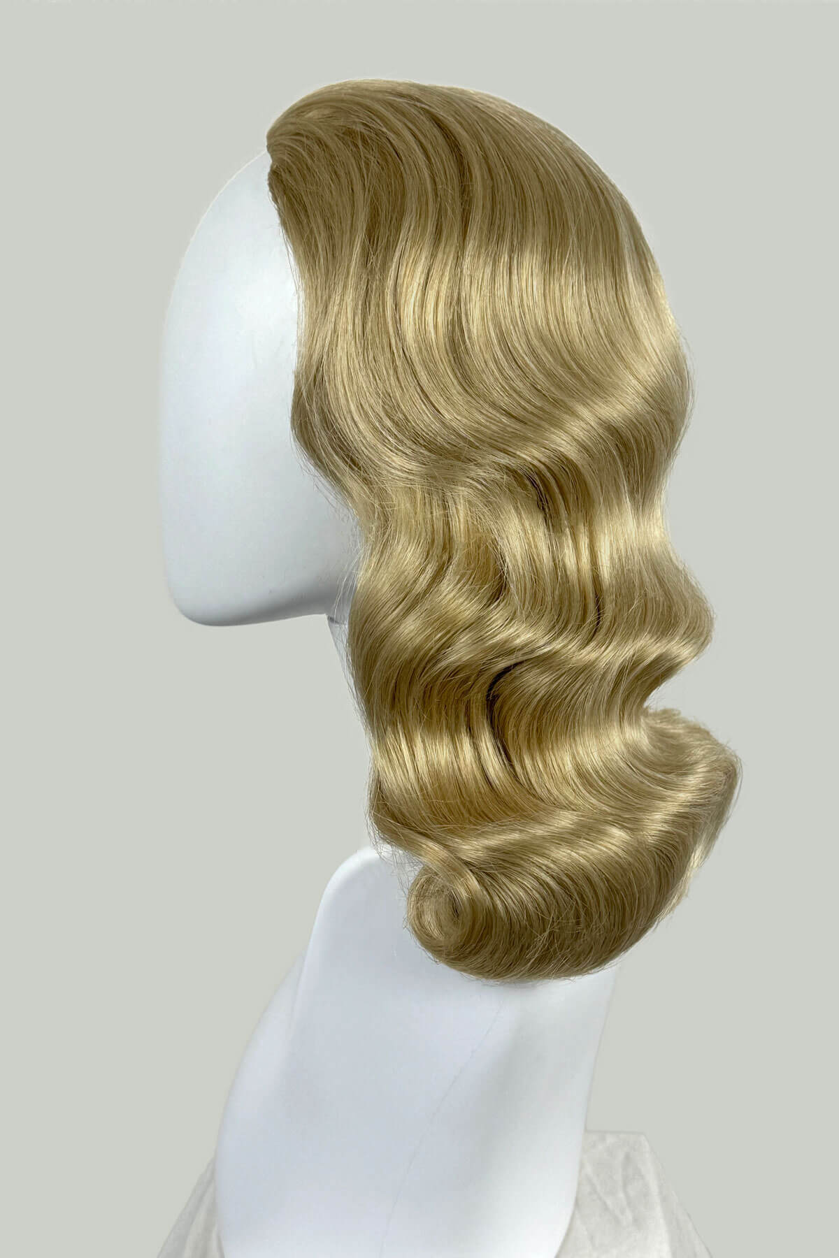 Blonde wig on a mannequin head against a plain background. 1950s style half wig hairpiece with deep finger waves: Deborah blonde 613T24