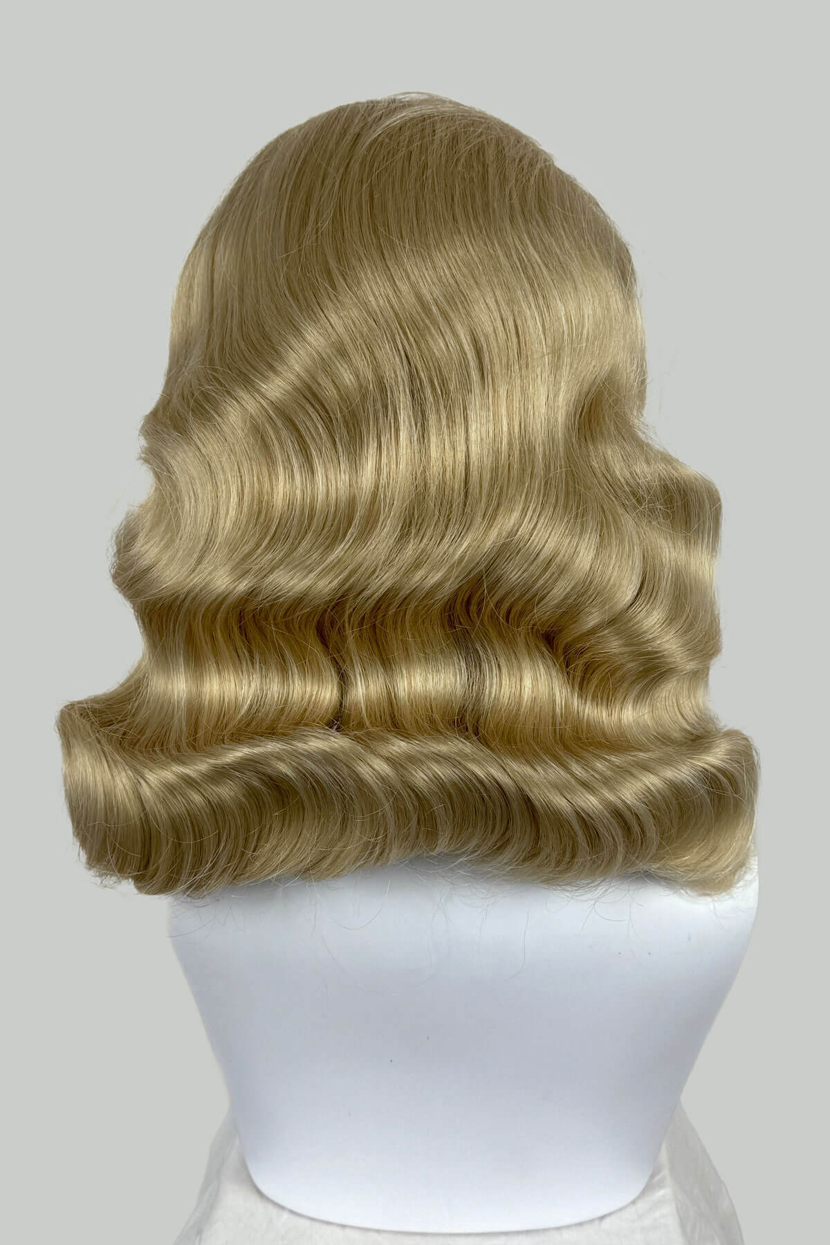 Blonde wig on a mannequin head against a plain background. 1950s style half wig hairpiece with deep finger waves: Deborah blonde 613T24