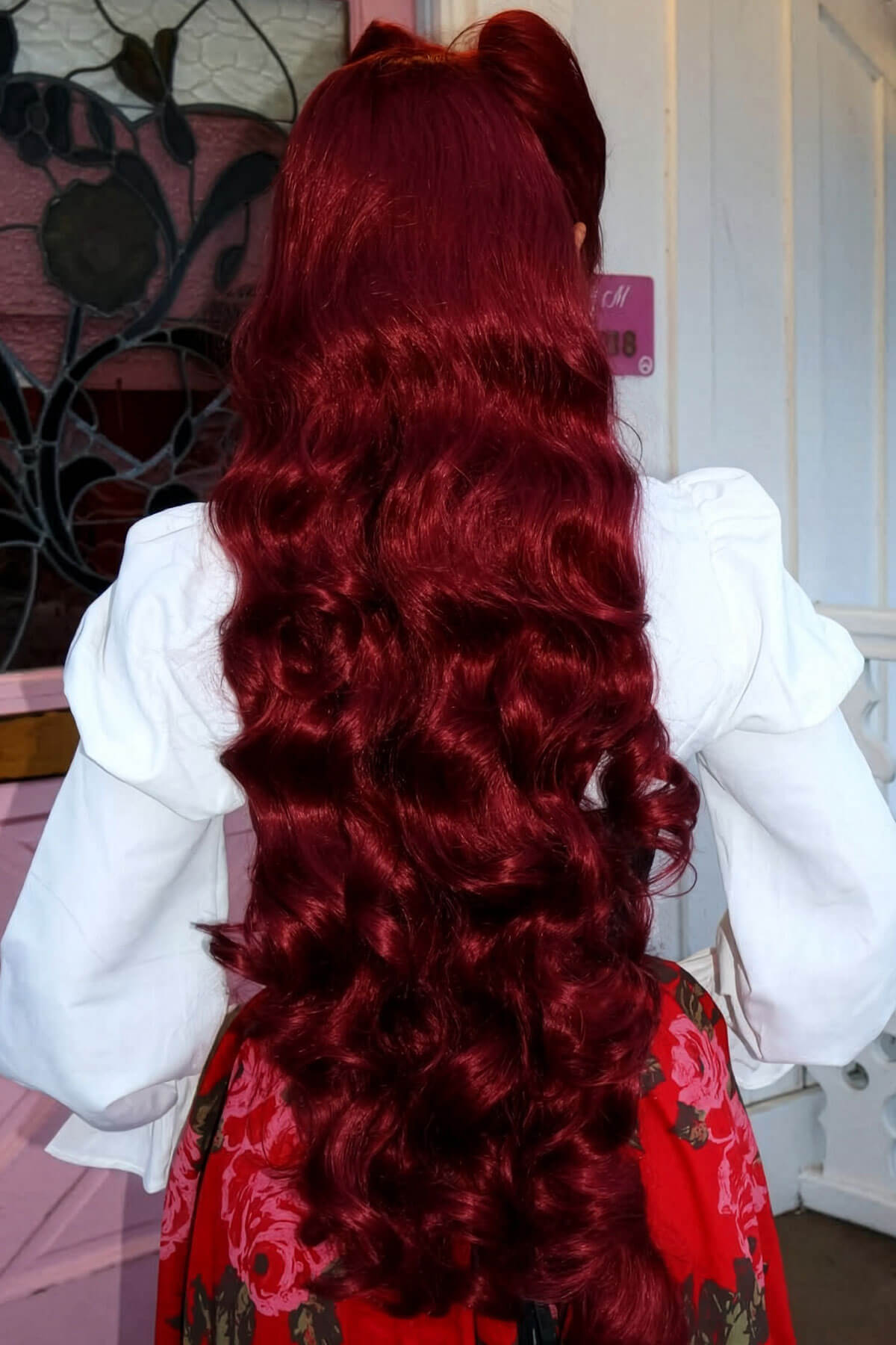 Person with red hair styled in a ponytail, wearing a white blouse and red floral skirt. Ultra long half wig with hollywood waves. cherry red 39