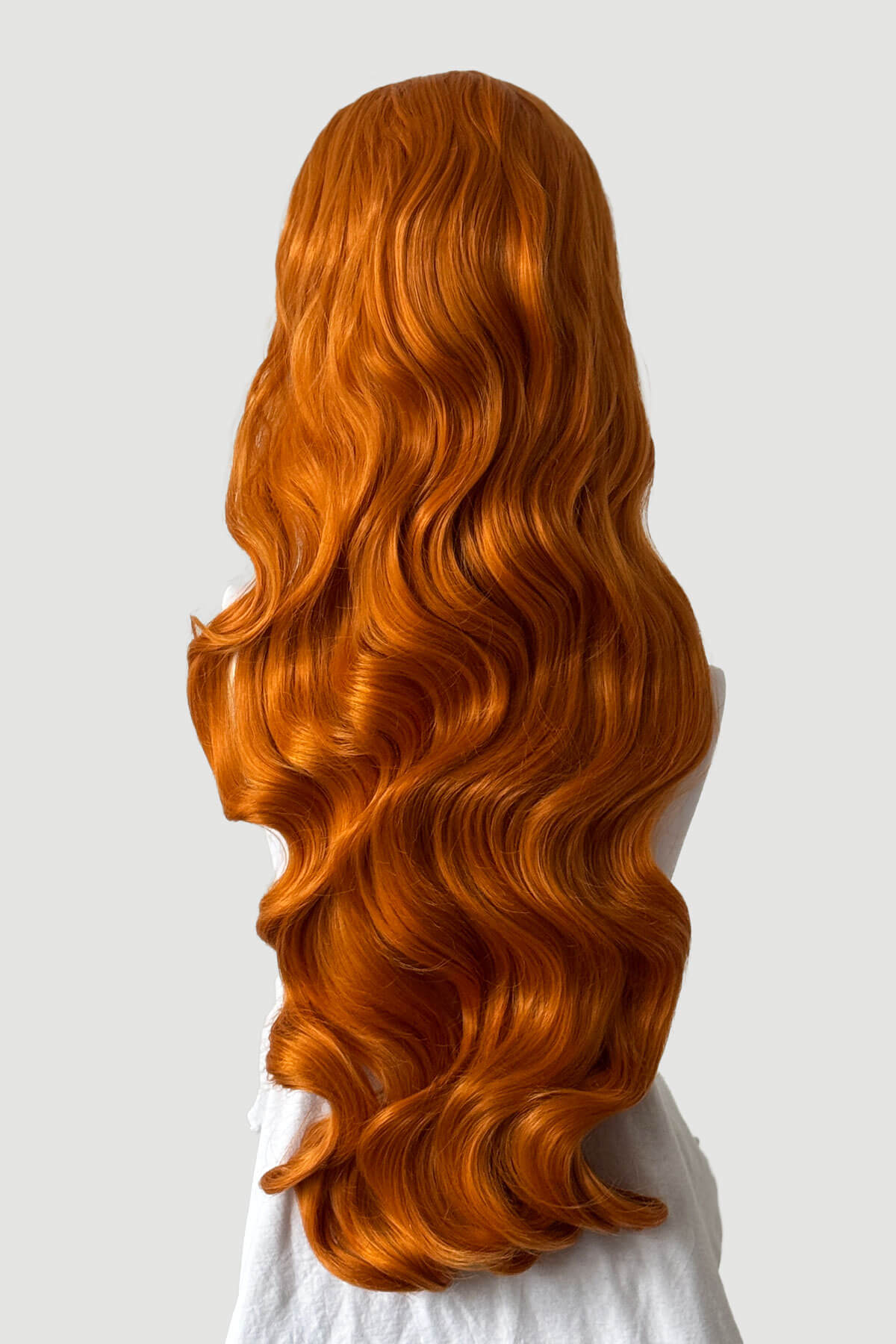 Mannequin head with long, ginger hair styled in a ponytail on a plain background. Ultra long half wig with hollywood waves. ginger