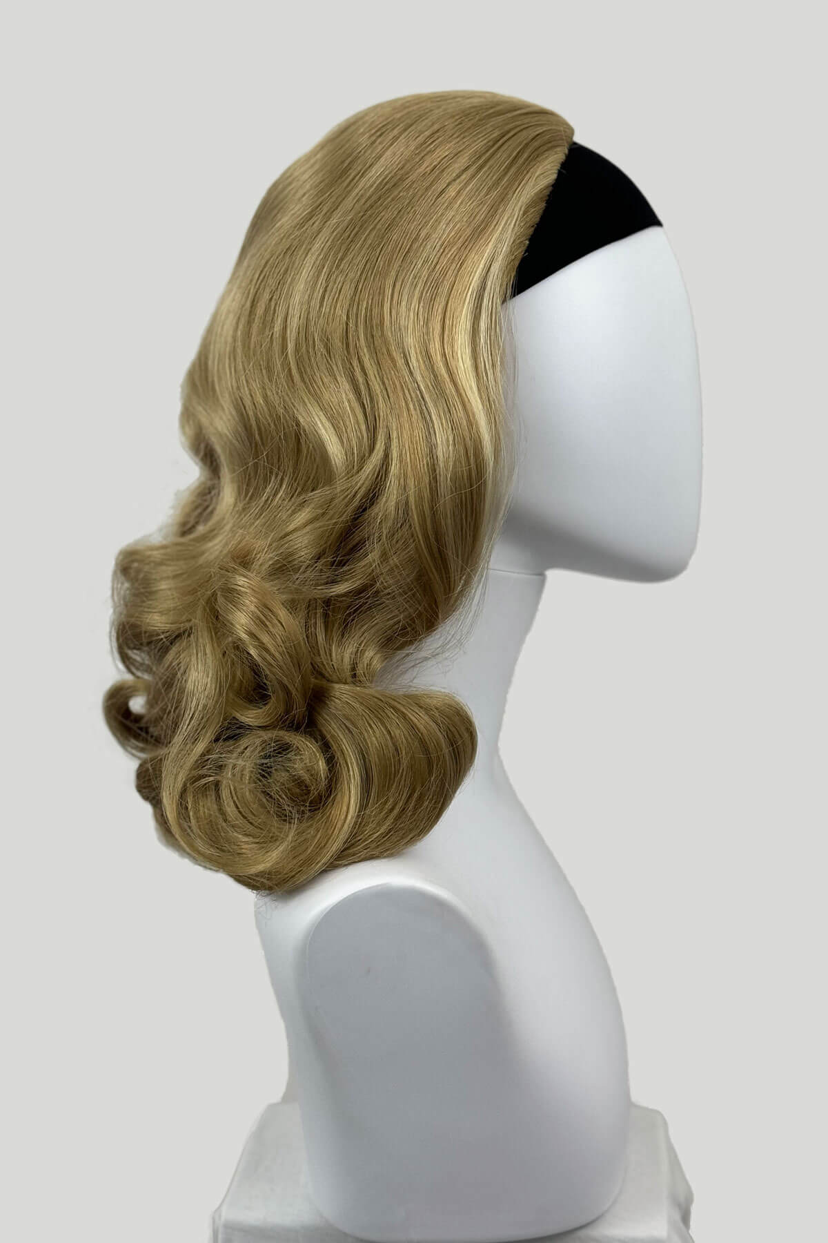 Blonde wig on a mannequin head against a white background shown from the side. 1950s style shoulder length half wig hairpiece with beautiful vintage waves: Onyx blonde 24H613