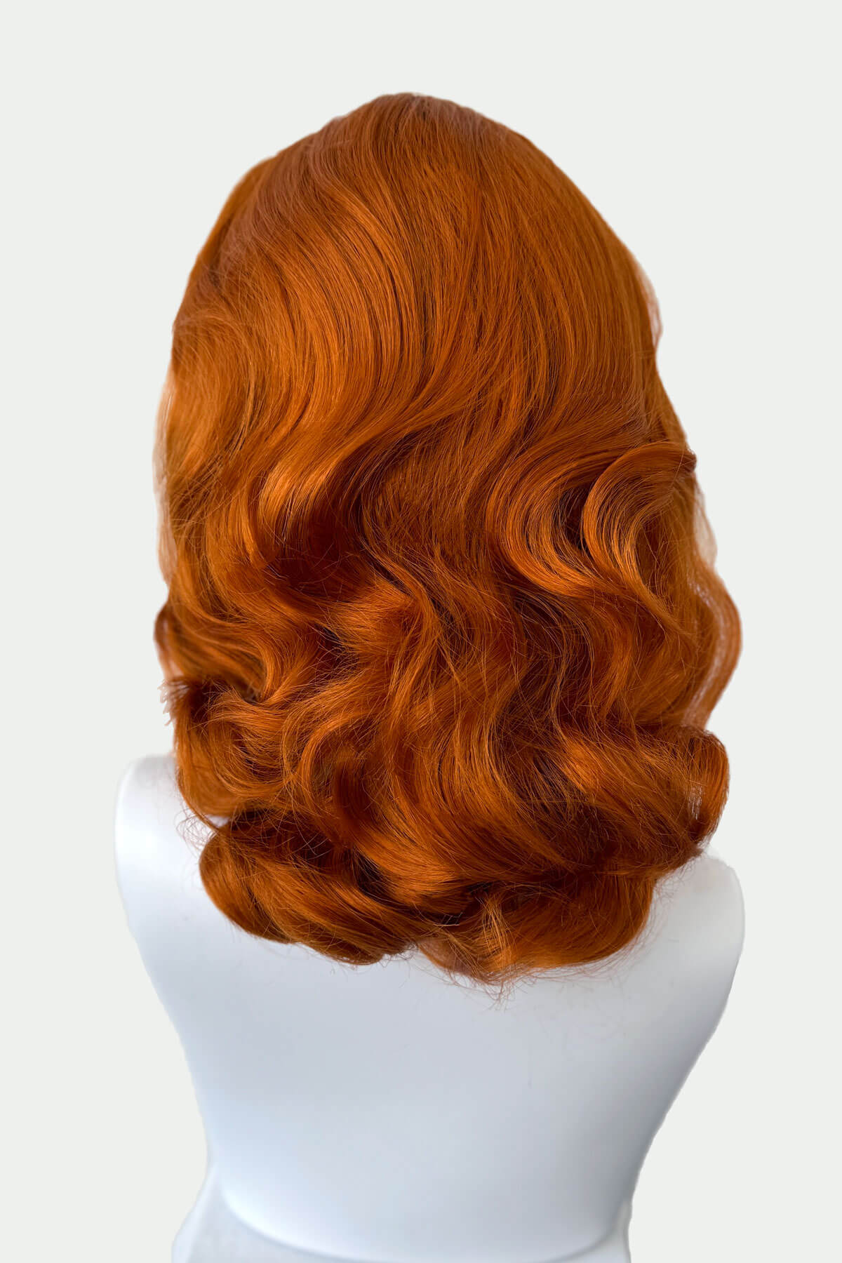 Ginger red wig on a mannequin head against a white background viewed from the back. 1950s style shoulder length half wig hairpiece with beautiful vintage waves: Onyx ginger