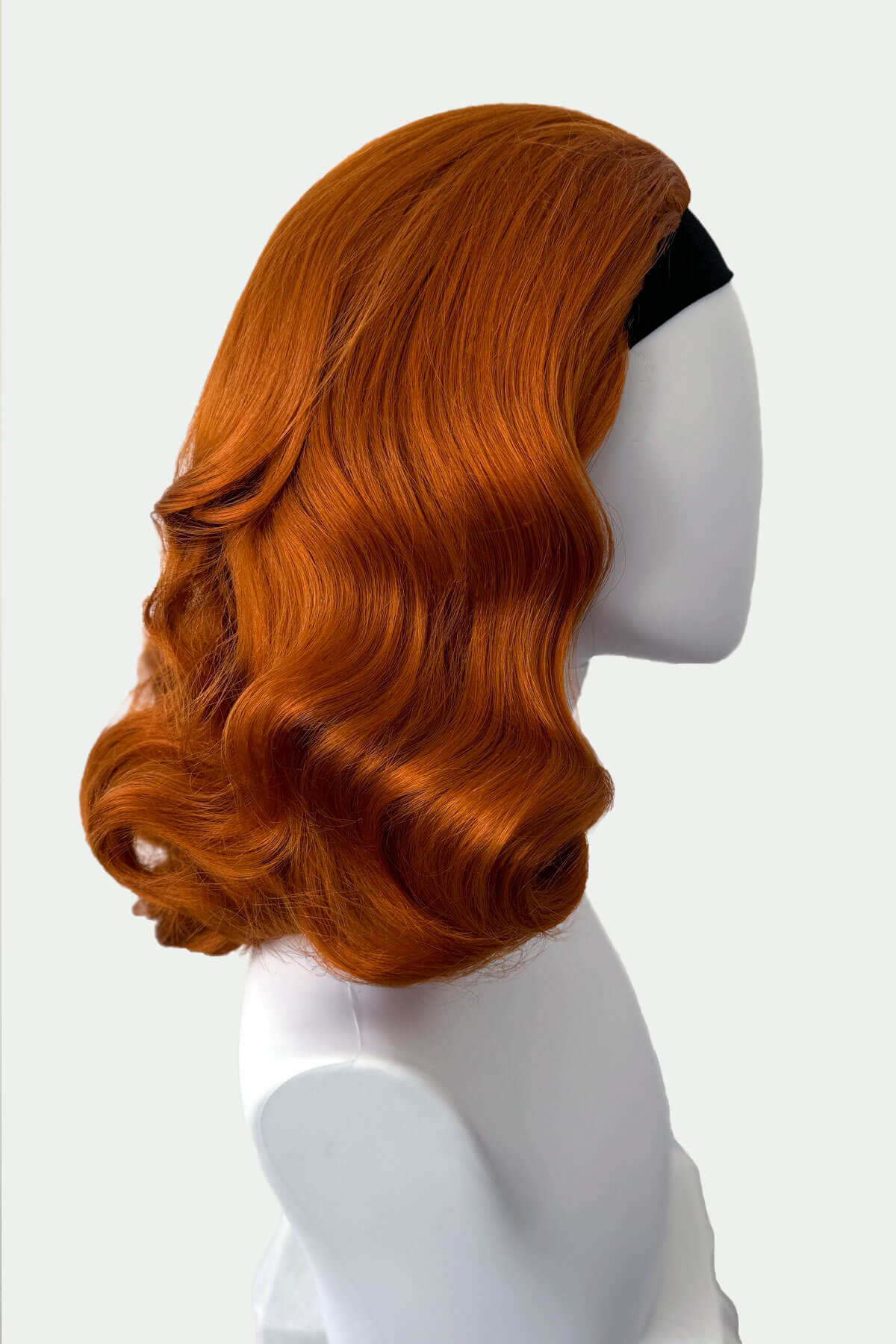 Ginger red wig on a mannequin head against a white background viewed from the side. 1950s style shoulder length half wig hairpiece with beautiful vintage waves: Onyx ginger
