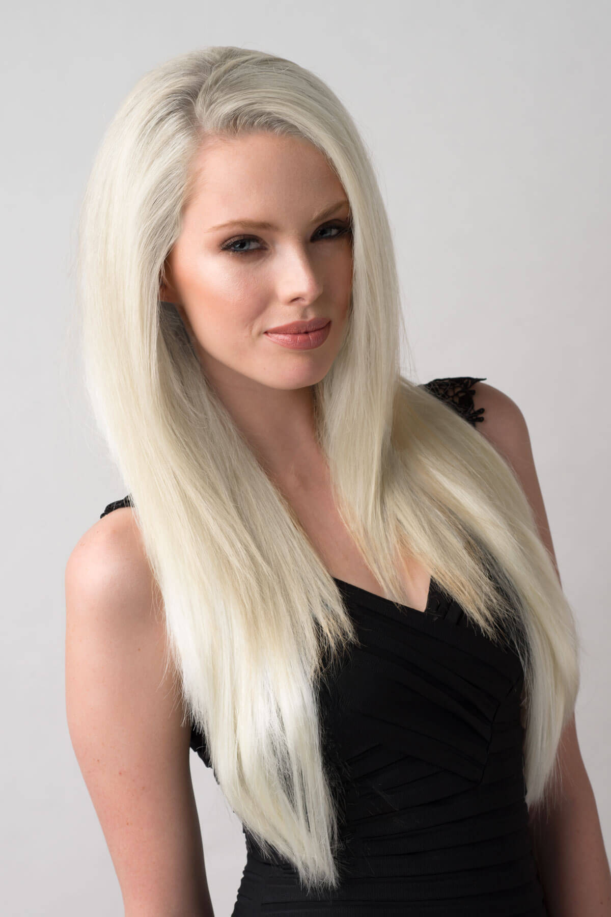 Woman with long blonde hair wearing a black top against a plain background. Straight platinum blonde half wig hairpiece (3/4 wig): Shannon