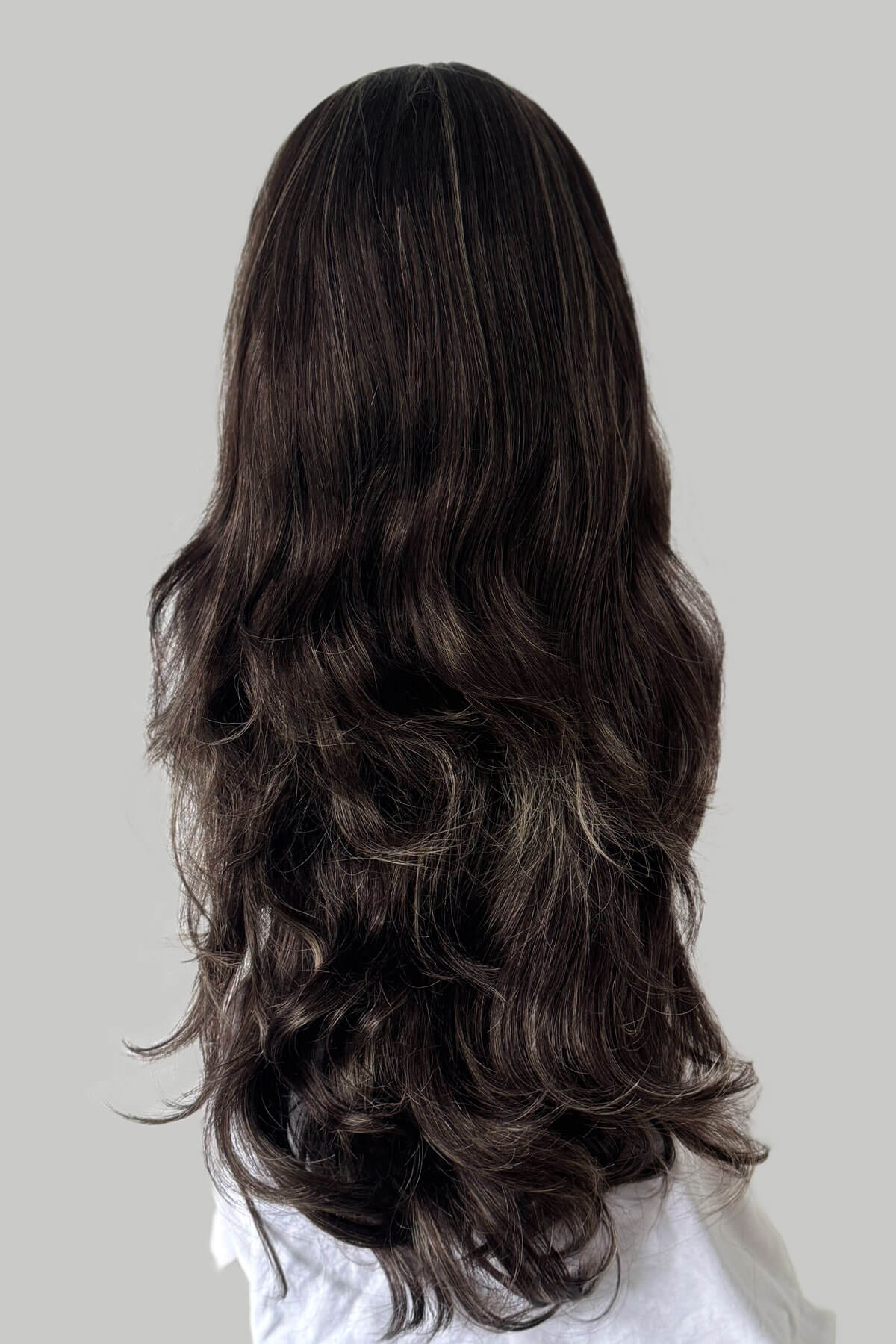 Long, wavy dark brown hair extension on a plain background. Brown half wig with blonde highlights: Reese 6H24