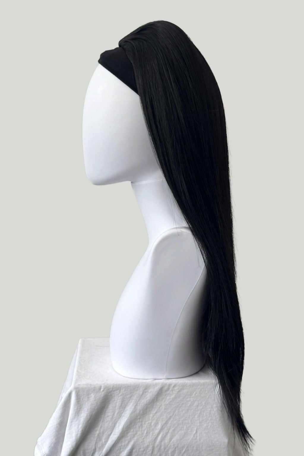 Black wig on a white mannequin head against a plain background. 1960s style hair, high crown long straight half wig: Andrea black 1B