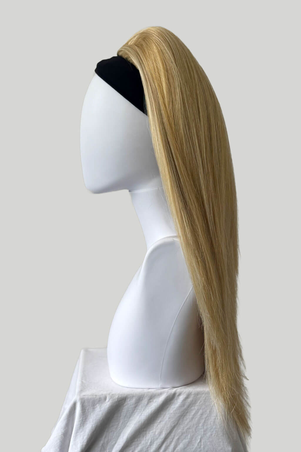 Blonde wig on a mannequin head against a plain background. 1960s style hair, high crown long straight half wig: Andrea blonde 24B613