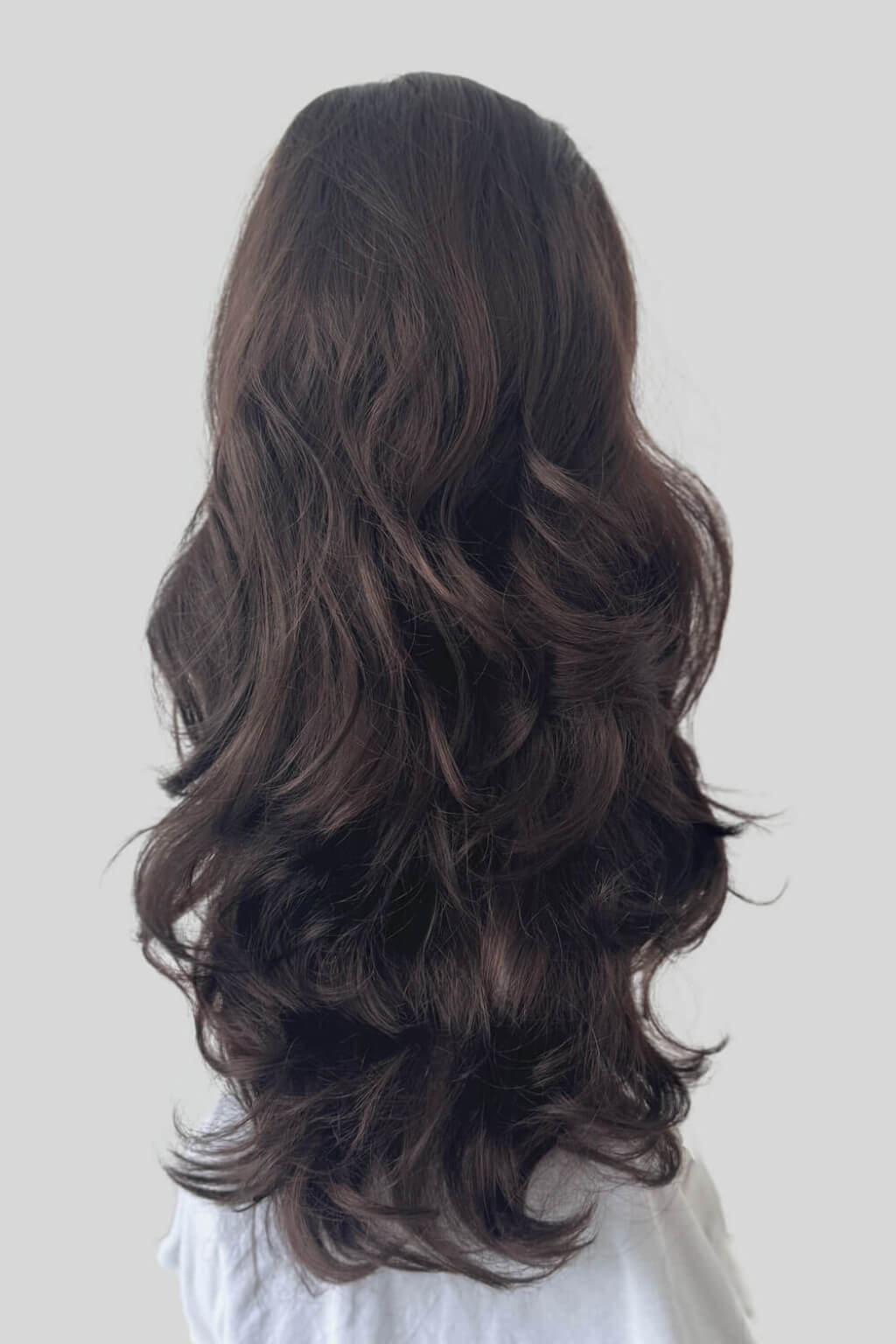 Long, wavy dark brown hair shown from the back on a model wearing a white top. High crown long, wavy half wig and volume ring: Bardot reddish brown 6-33