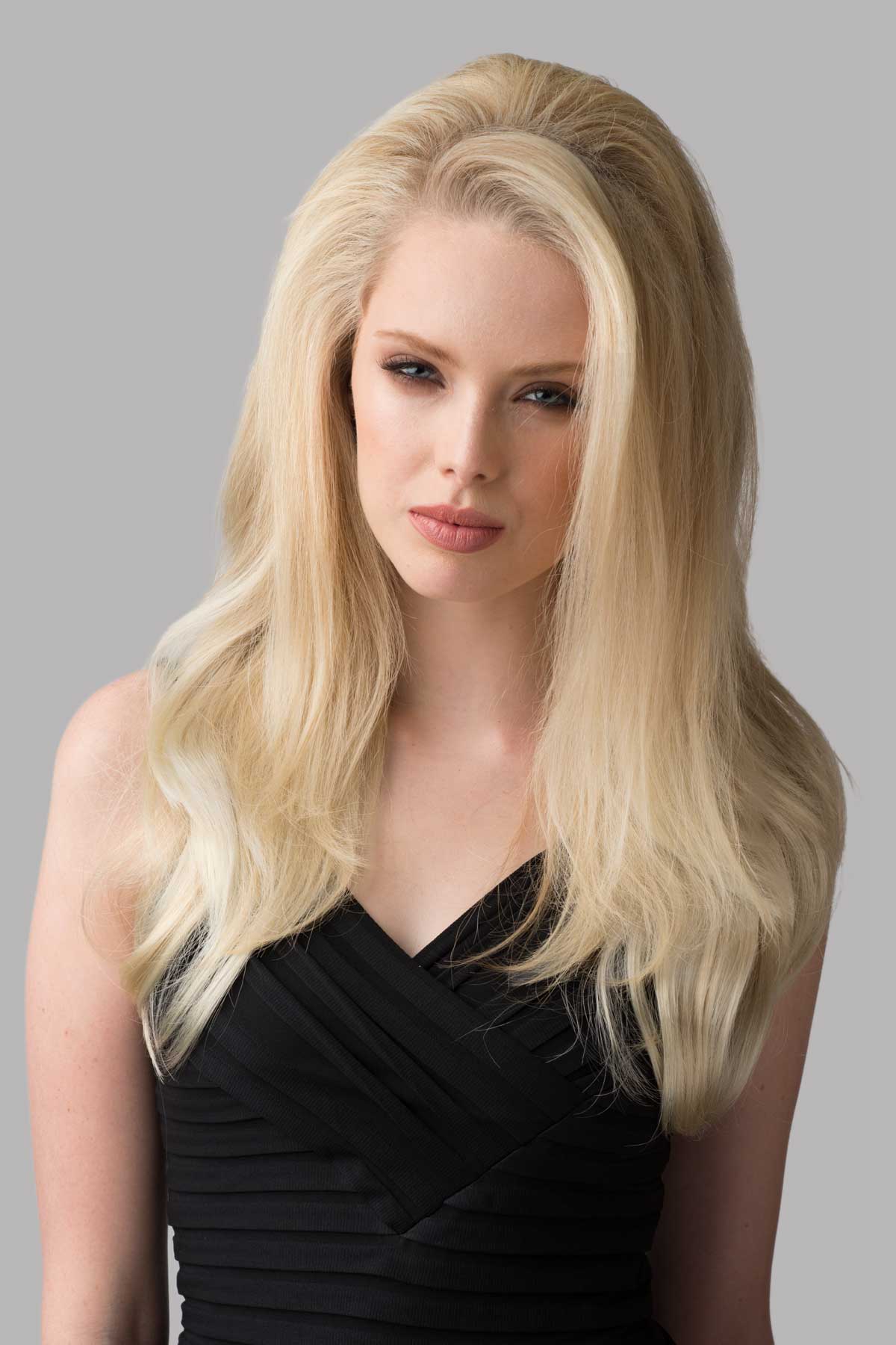 Woman with long blonde hair wearing a black dress against a gray background