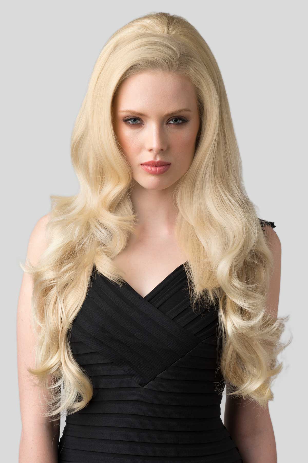 Woman with long blonde hair wearing a black dress on a gray background. Half wig with volume booster/height booster: Corrine