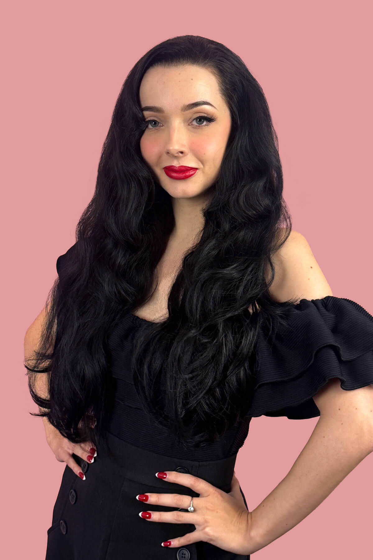 Woman with long black wavy hair and red lipstick posing against a pink background. Black half wig hairpiece (3/4 wig), long layers: Aislynn black 1B