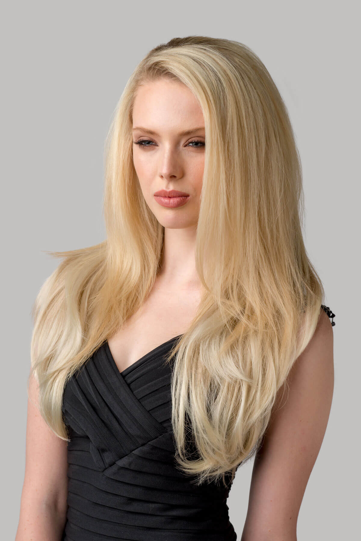 Woman with long blonde hair wearing a black dress against a gray background. Straight blonde half wig hairpiece (3/4 wig), layered: Autumn ash blonde to light blonde 613T24