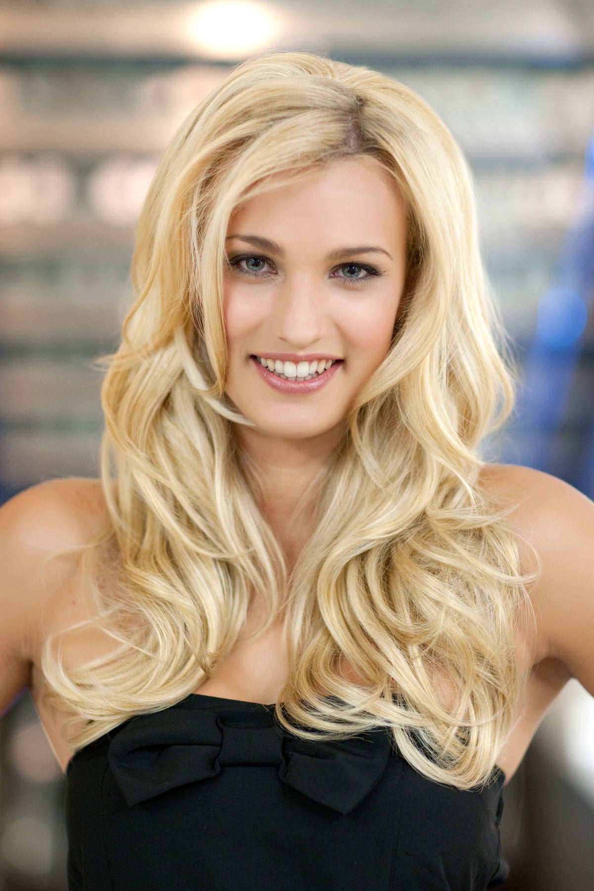 Woman with long blonde hair wearing a black top against a blurred indoor background