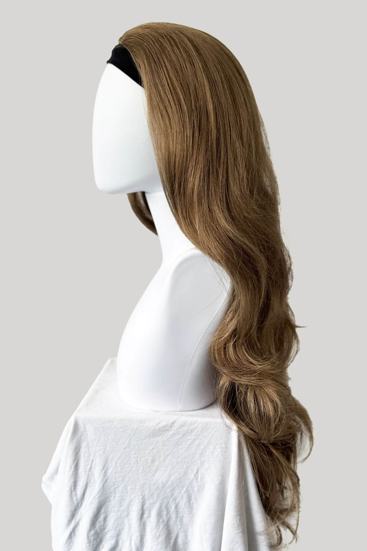 Mannequin head with a long, wavy brown wig on a plain background. Light golden brown half wig hairpiece, wavy: Teresa