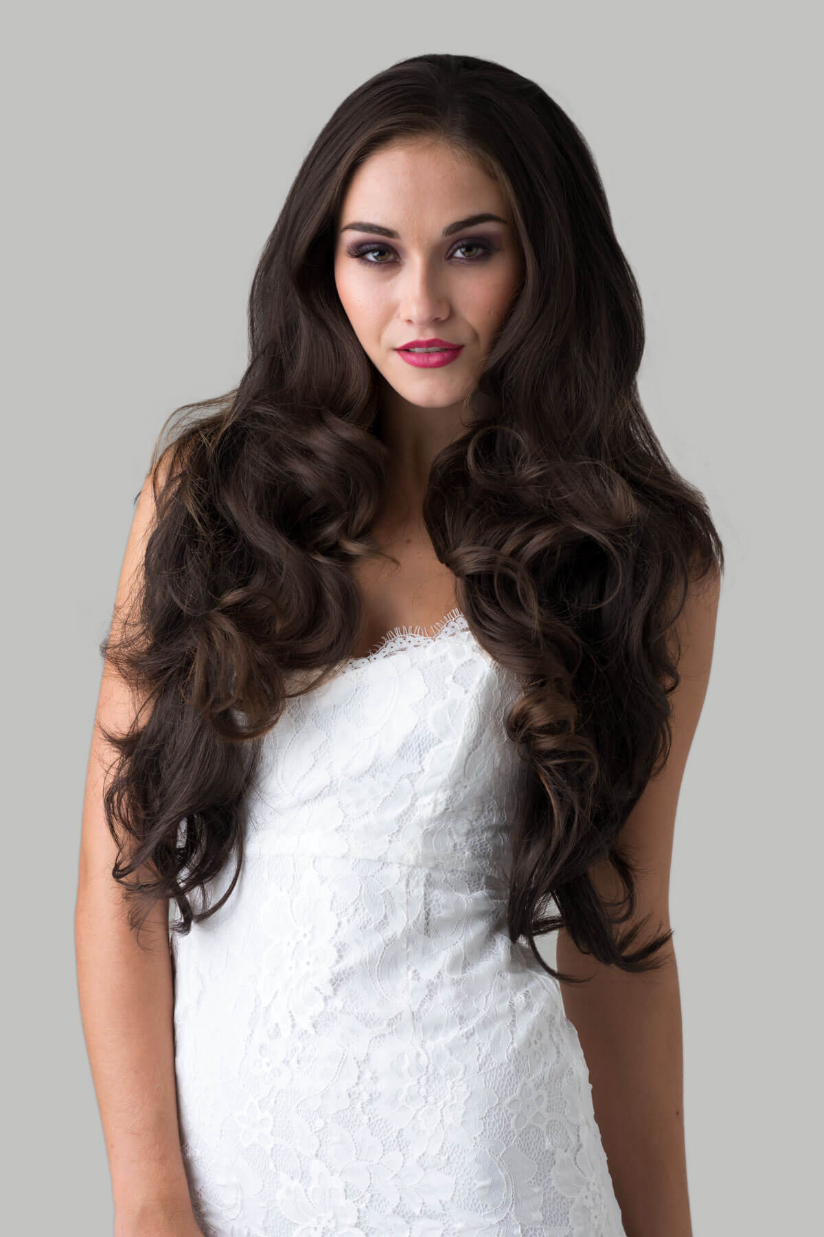 Woman with long, wavy brown hair wearing a white dress against a gray background. Brown half wig hairpiece, full, long with gentle waves: Taya dark chocolate brown 6